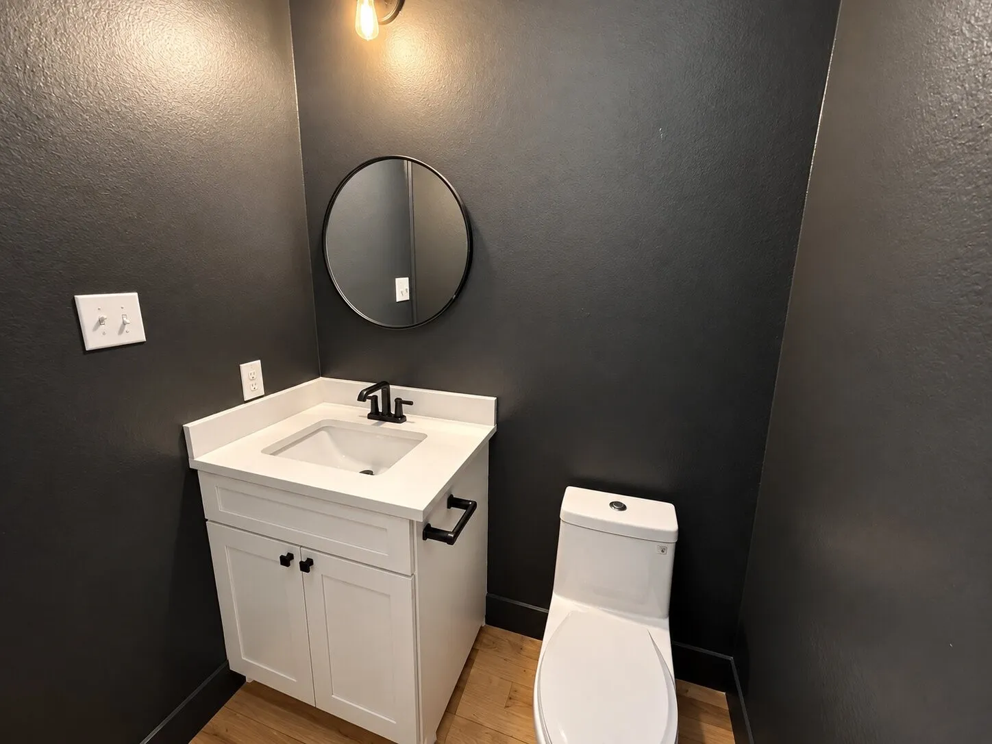 White vanity with an integrated sink, matte black faucet, and a circular wall mirror