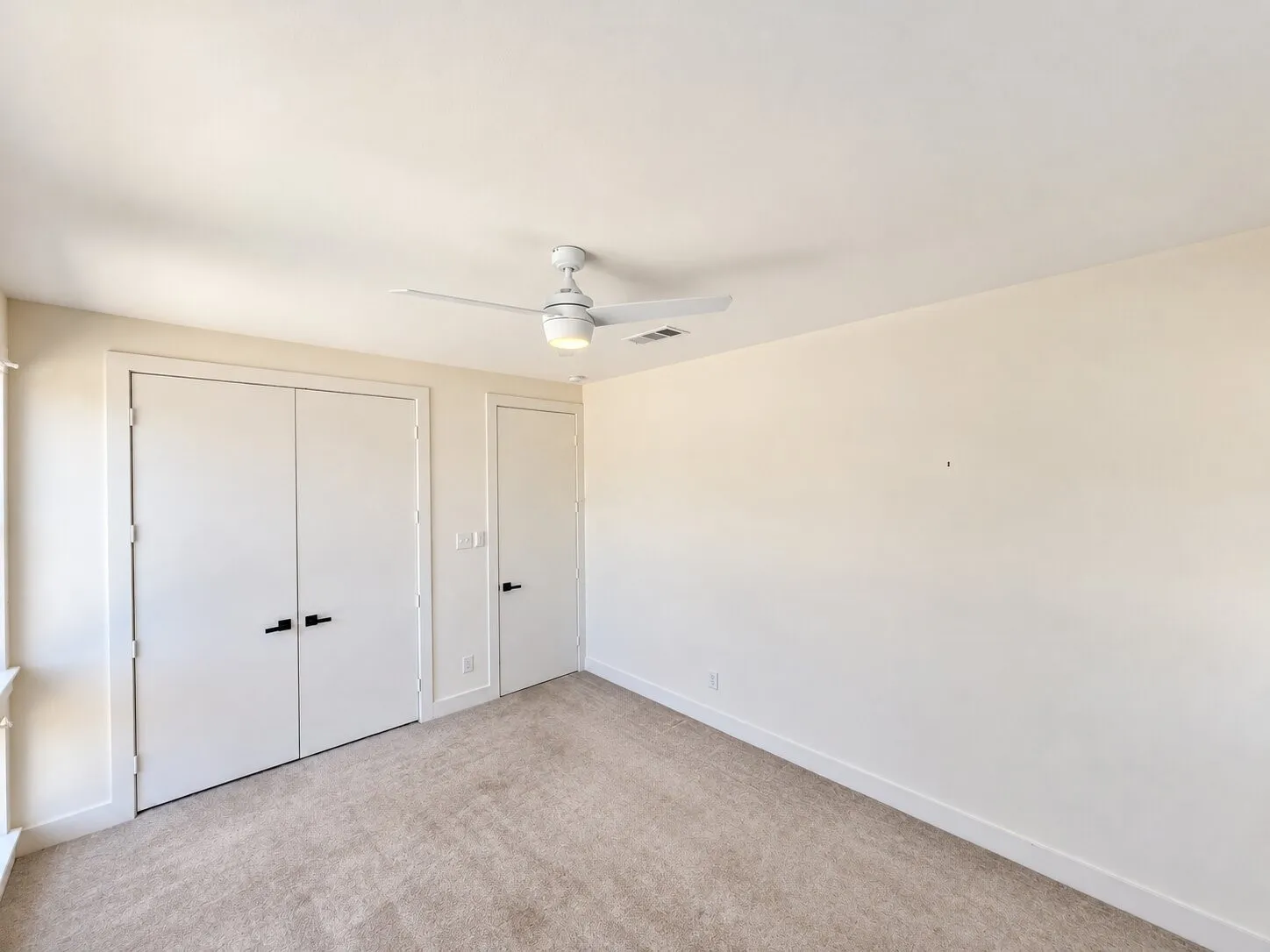 Beige carpeted flooring, white ceiling, white walls, white trim, matte black door hardware, ceiling fan with integrated lighting