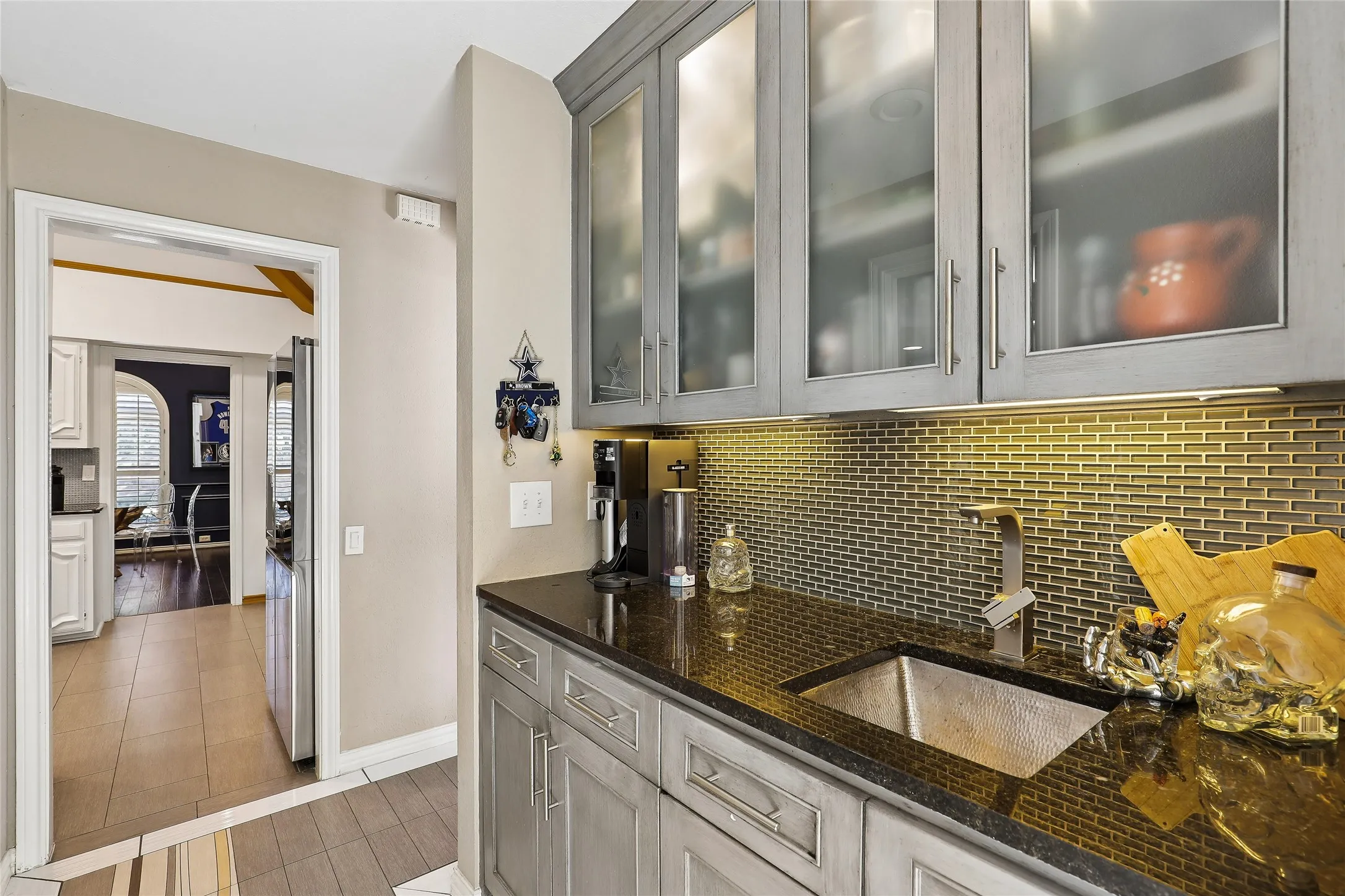 Wet bar with gray cabinetry, luxury granite, frosted glass upper cabinet doors, and a hammered copper sink.  Also includes huge wine fridge and custom tile flooring.
