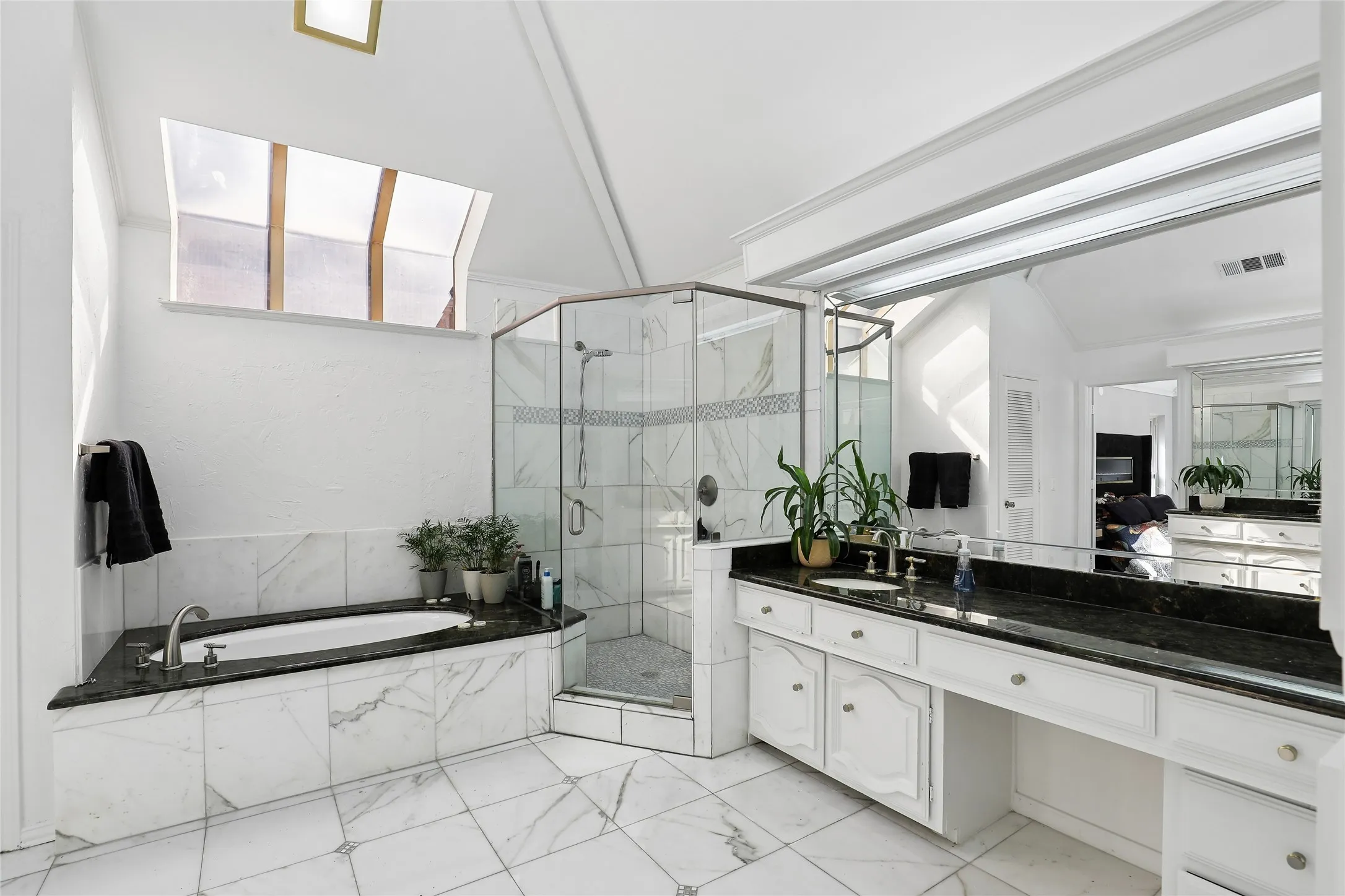 Just stunning! Vaulted ceiling with skylight, marble tiled flooring, built-in soaking tub with dark countertop, glass-enclosed shower, and dual vanity with dark granite countertops