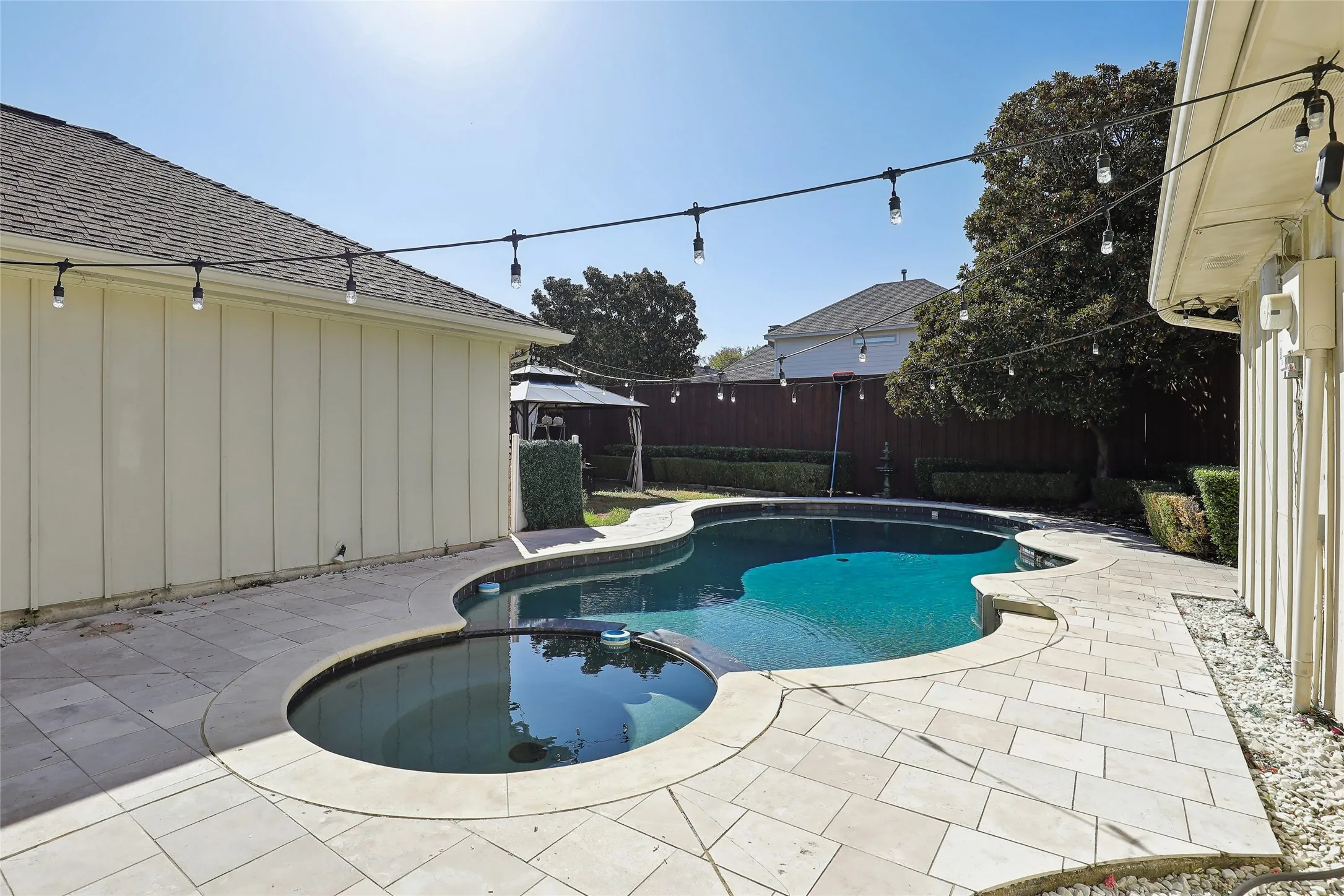 Freeform swimming pool with integrated spa and surrounding paver patio