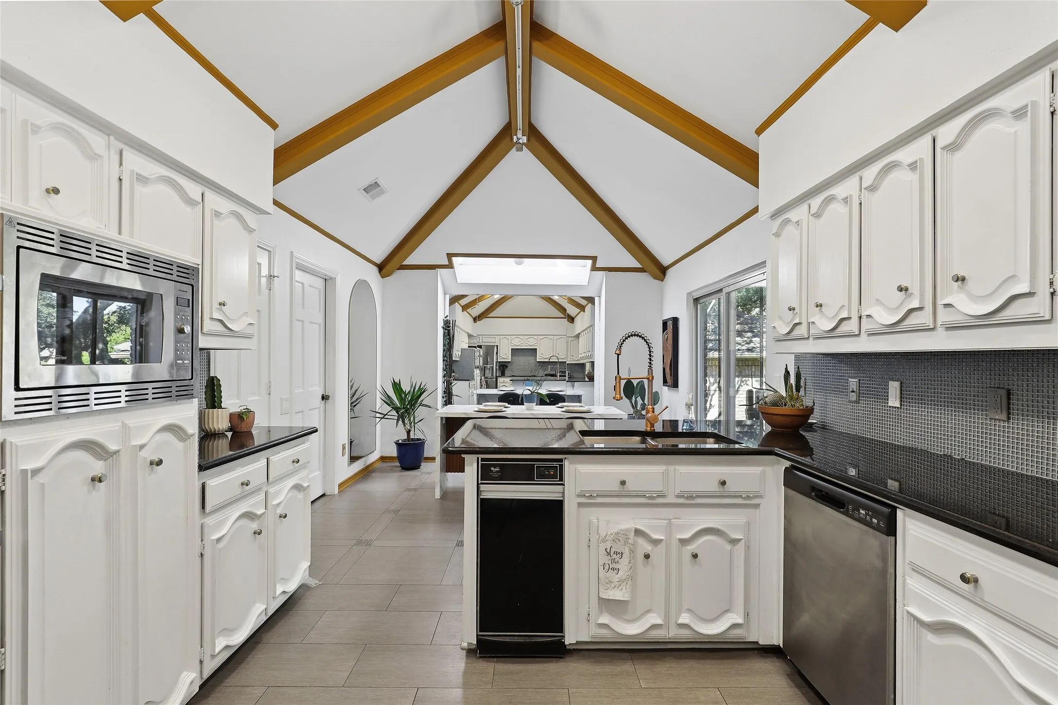 Vaulted ceilings with exposed wood beams, white cabinetry, dark countertops, built-in stainless steel microwave, and tile flooring