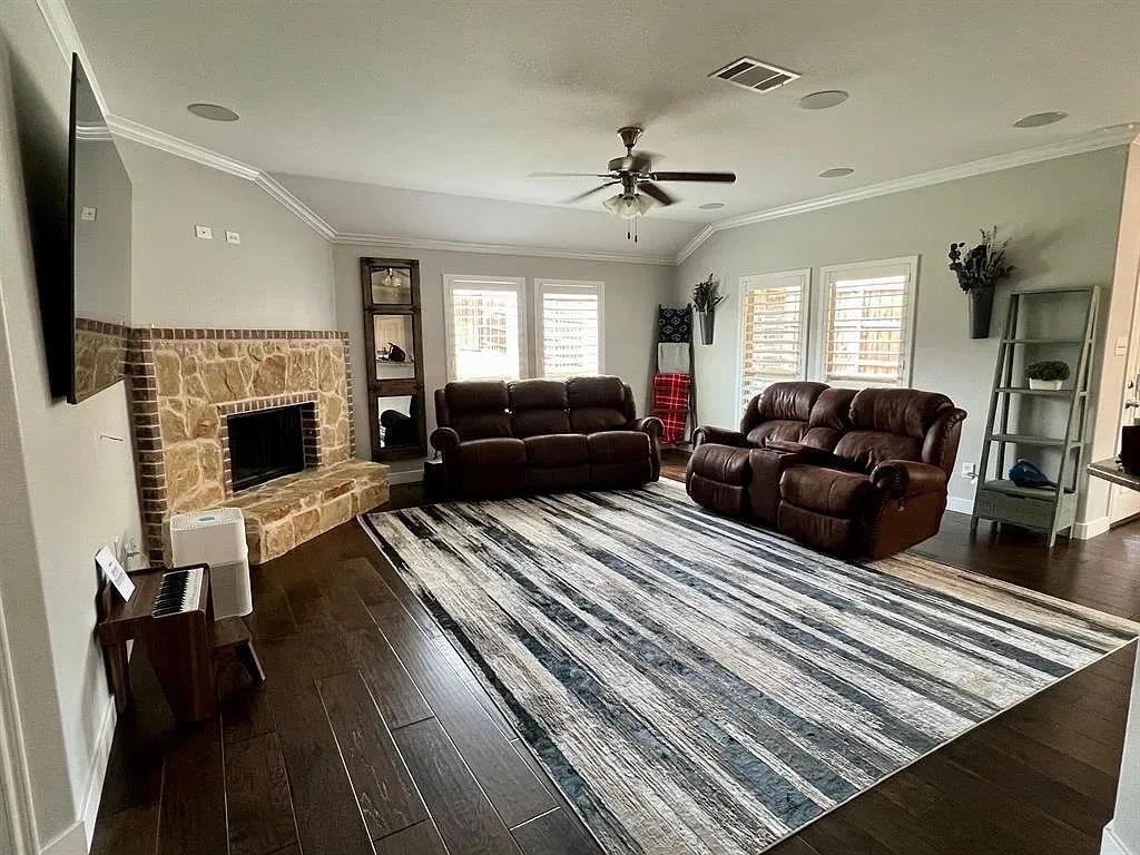 Spacious living area featuring a stone and brick fireplace, vaulted ceiling with a ceiling fan, and dark wood-finish flooring