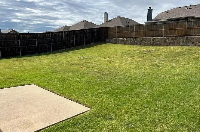 Expansive green lawn with a concrete patio, wood privacy fencing, and a stone retaining wall