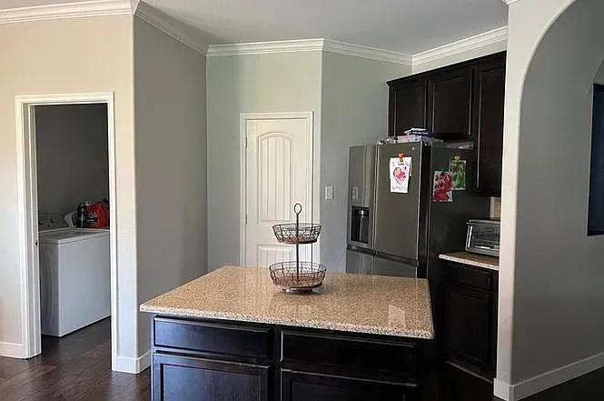 Kitchen island with a light-toned speckled countertop, dark wood-finish cabinetry, stainless steel refrigerator, and wood-finish flooring