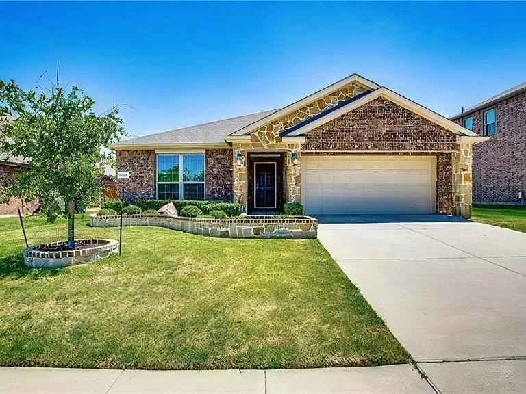 Brick and stone facade, attached two-car garage, concrete driveway, front yard landscaping with stone border, and a mature tree