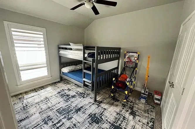 Pitched ceiling, window with plantation shutters, ceiling fan, and paneled door