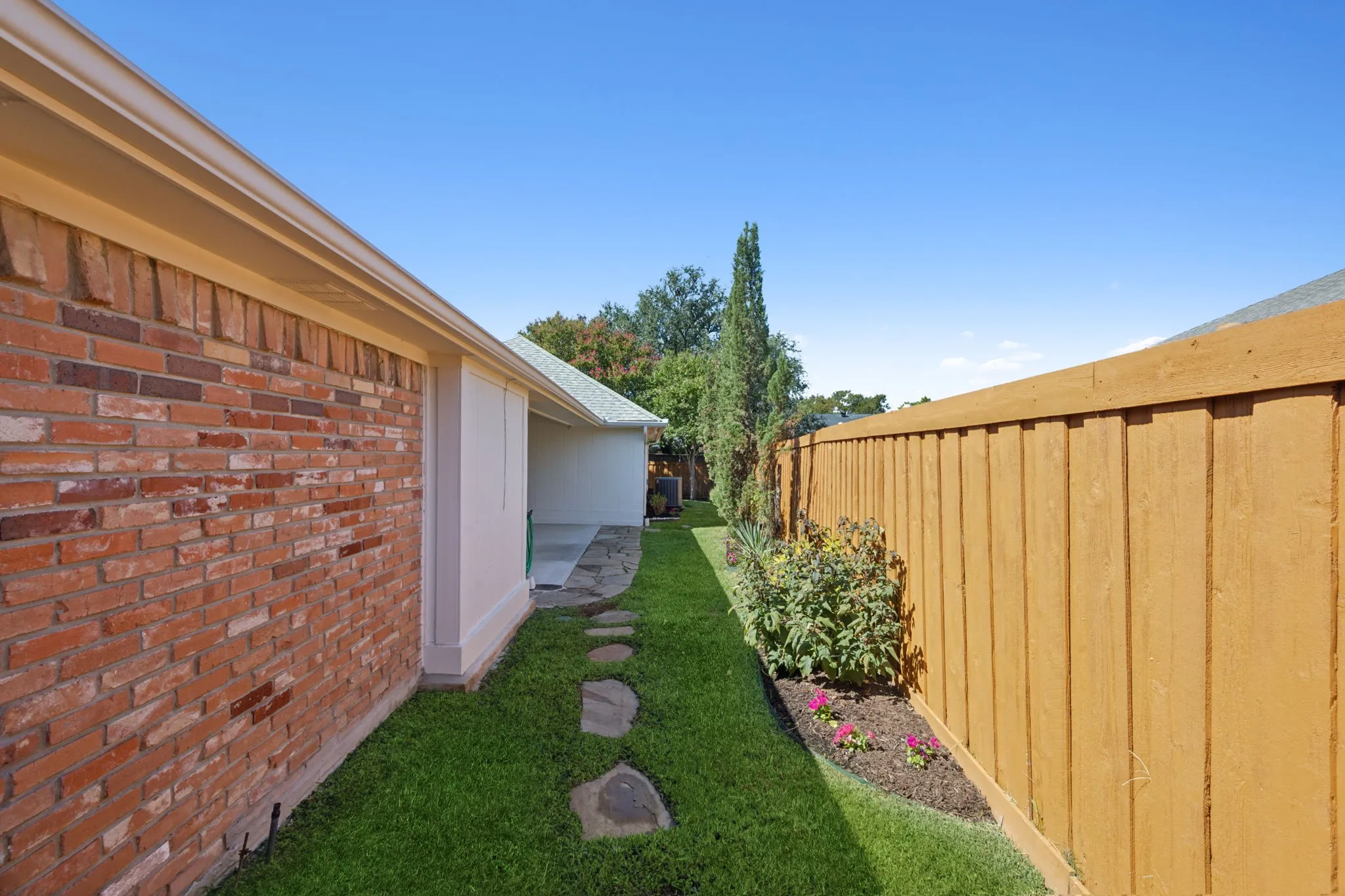 Manicured lawn with stepping stones, brick exterior, and a wood privacy fence