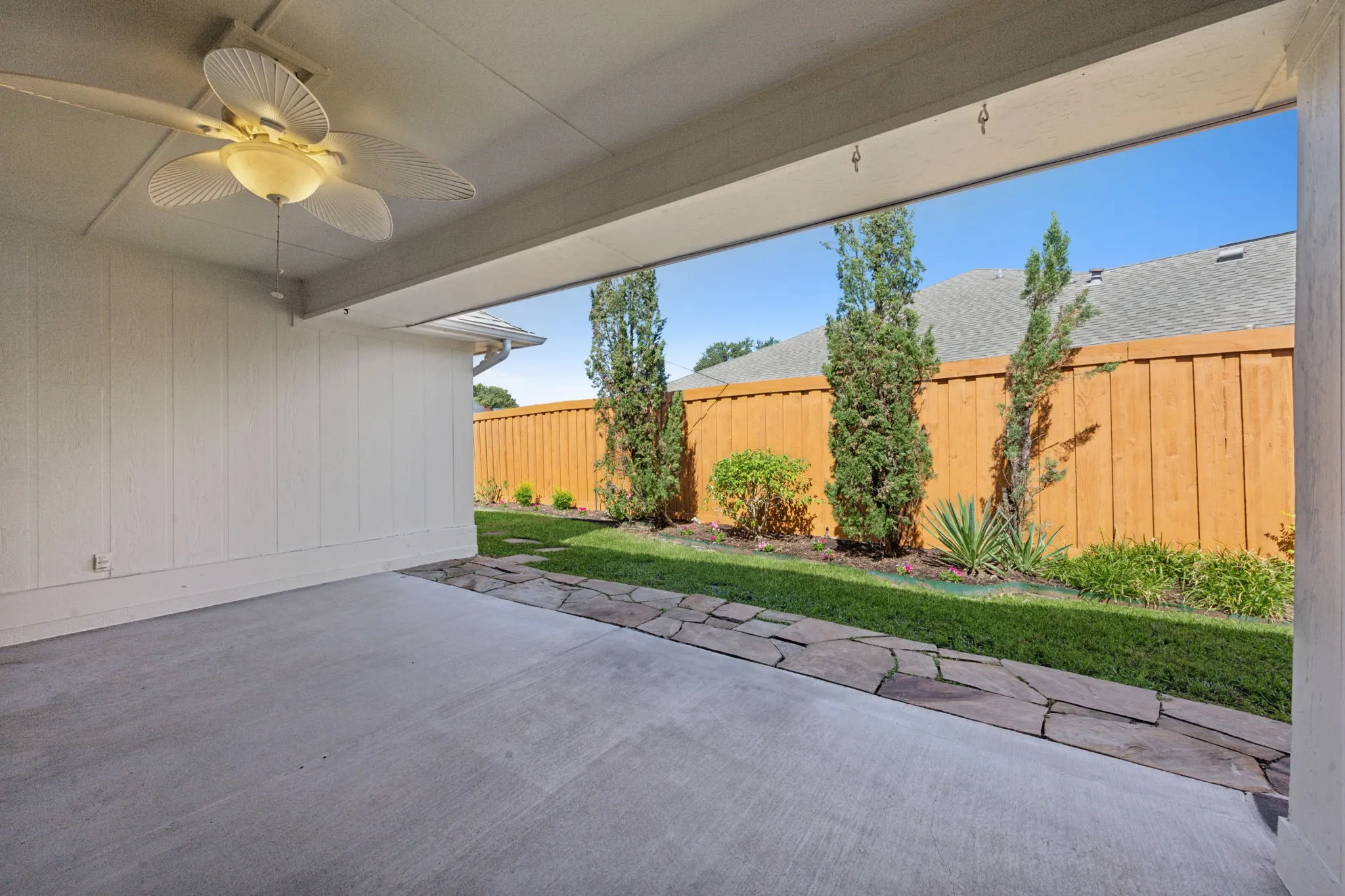 Covered patio with a ceiling fan, concrete flooring, and a stone walkway