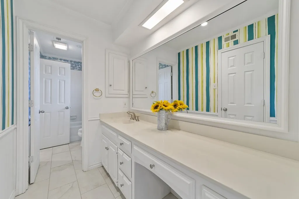 Extended vanity featuring a built-in dressing area, white cabinetry with silver-tone hardware, and a single basin with a chrome faucet