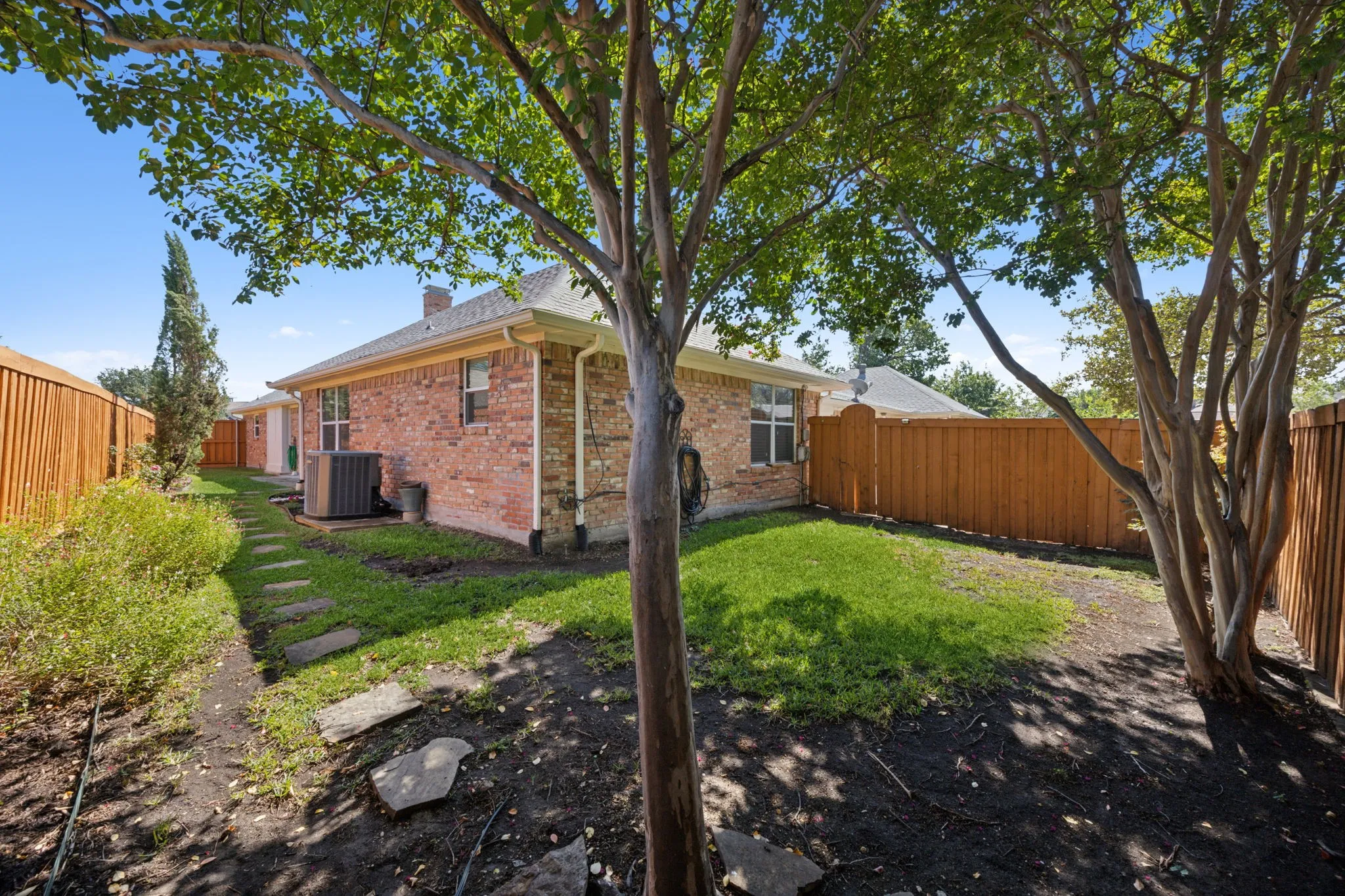 Private backyard with mature trees, a manicured lawn, and a stone-paver walkway, fully enclosed by a wood privacy fence