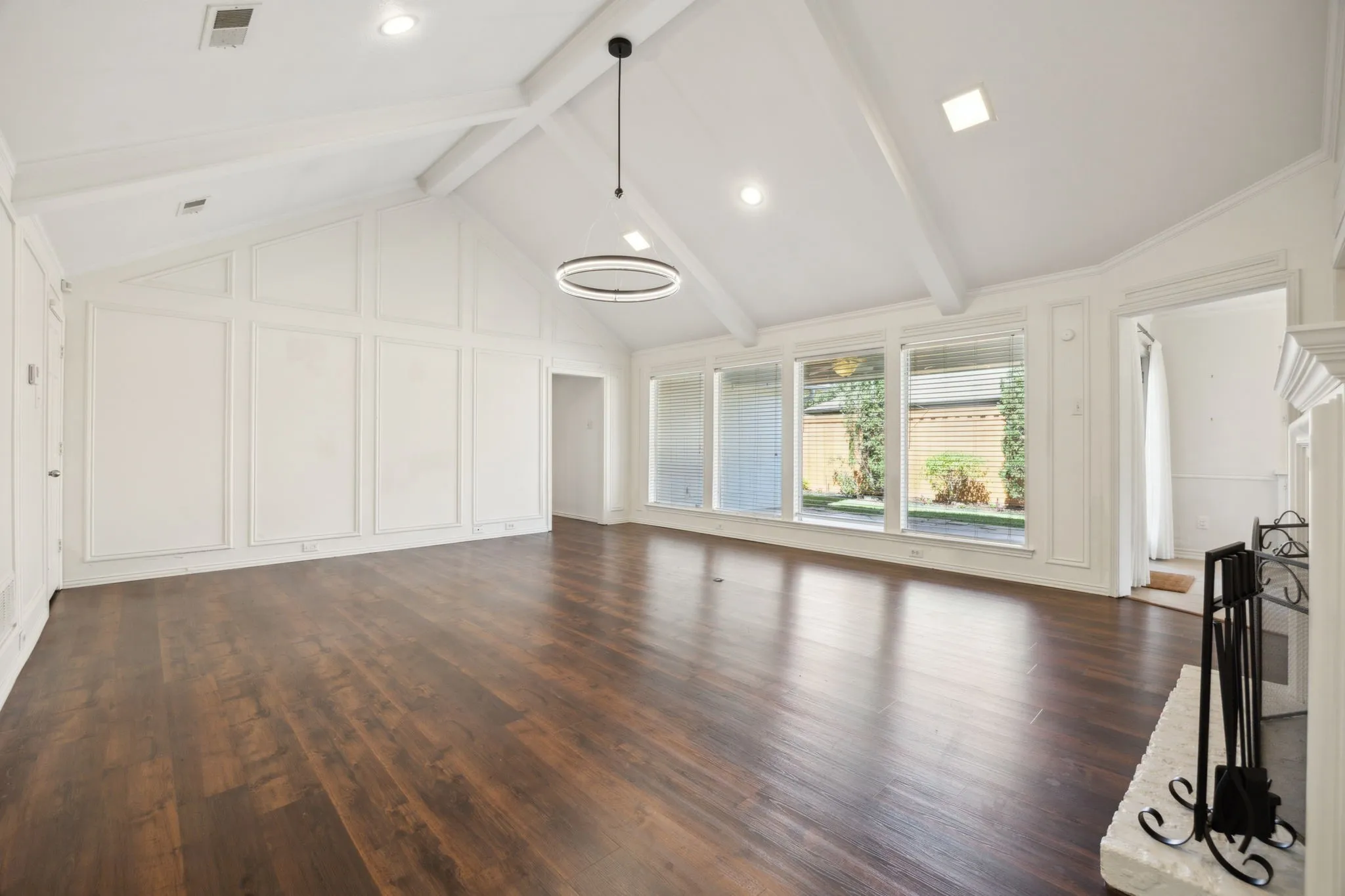 Vaulted ceiling with exposed beams, wood-finish flooring, accent wall paneling, modern circular chandelier, and a decorative fireplace surround