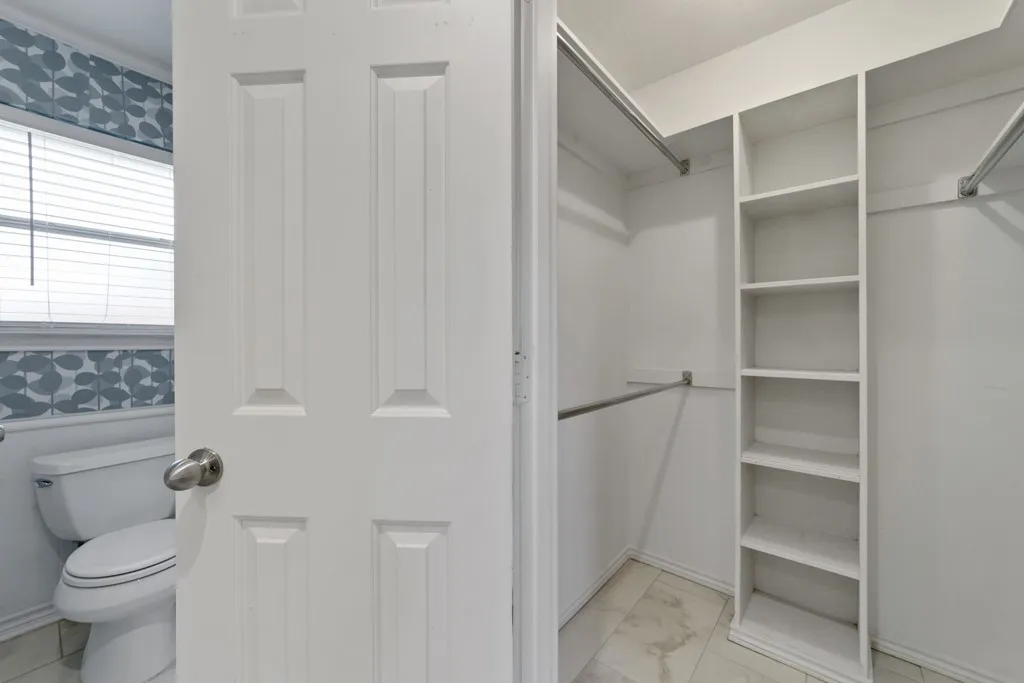 Walk-in closet with built-in shelving, two hanging rods, and light-toned flooring