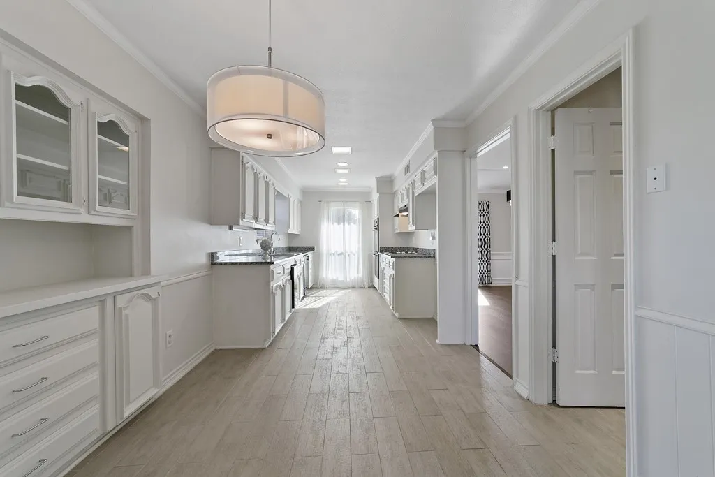 Galley kitchen featuring wood-finish flooring, white cabinetry, dark countertops, and a built-in buffet