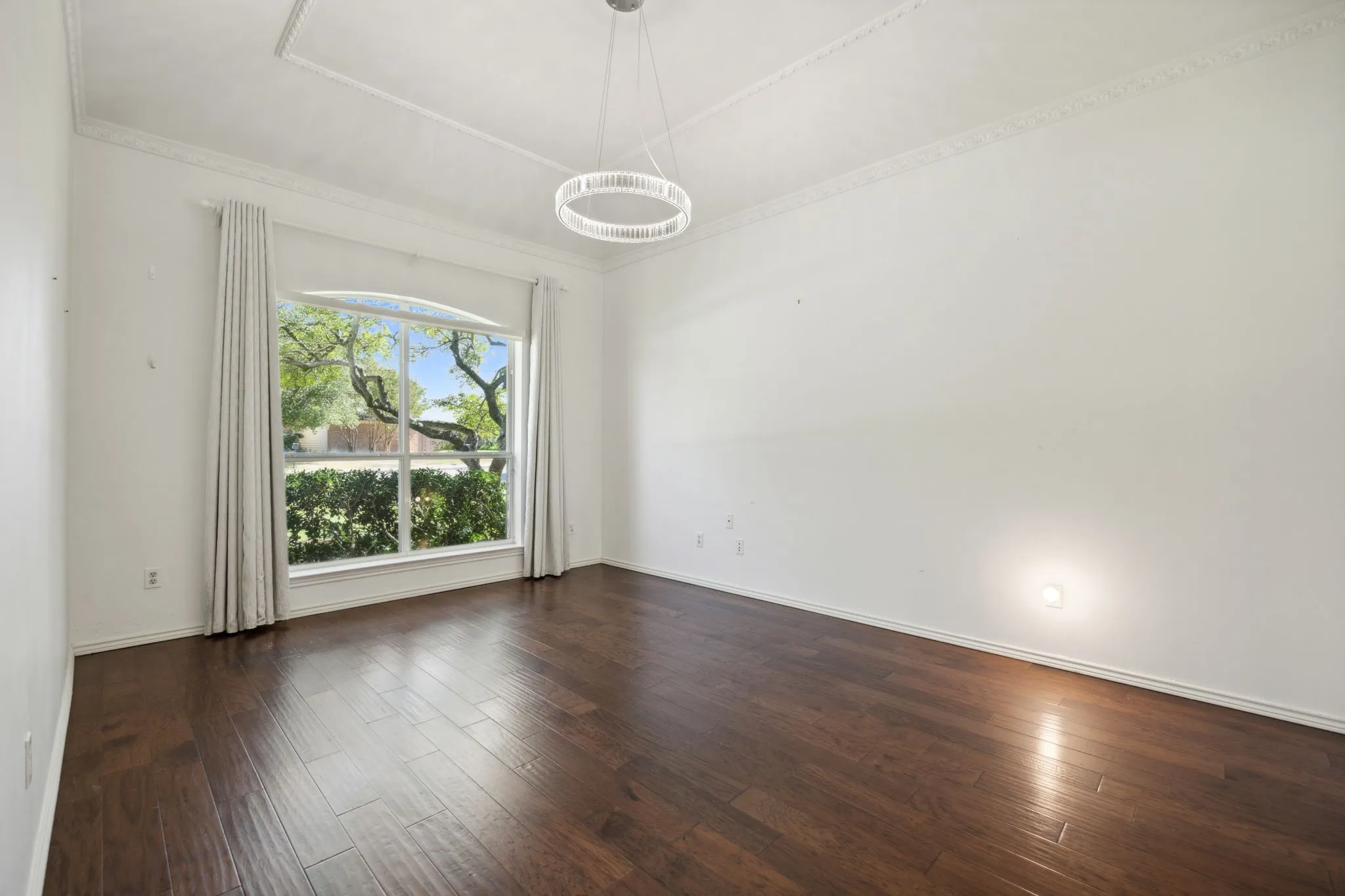 Hardwood flooring, crown molding, tray ceiling, contemporary chandelier, and large arched window