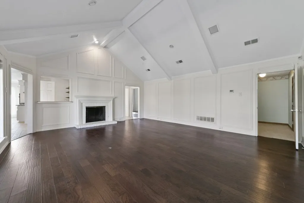 Vaulted ceilings with exposed beams, dark wood-finish flooring, white paneled walls, a fireplace with a mantel, and a pass-through window with a built-in shelf