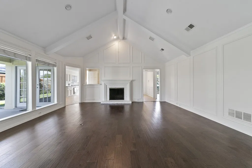 Vaulted ceiling with exposed beams, dark wood-finish flooring, white fireplace with hearth, and French doors