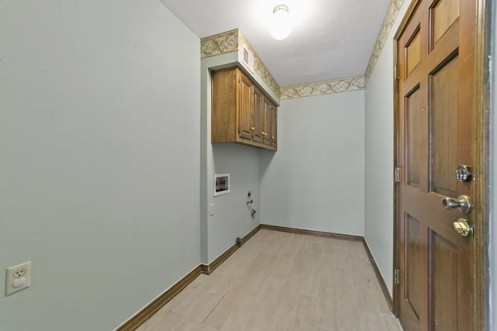 Wood-finish plank flooring, overhead cabinetry, and a panel-style door with metal hardware