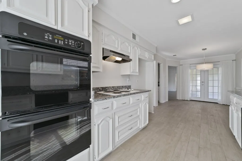 White cabinetry with dark hardware, built-in double oven, and granite-style countertops