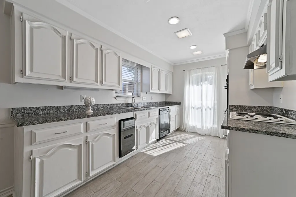 White cabinetry with decorative arch panels, speckled countertops, stainless steel sink, built-in cooktop with range hood, and wood-finish flooring