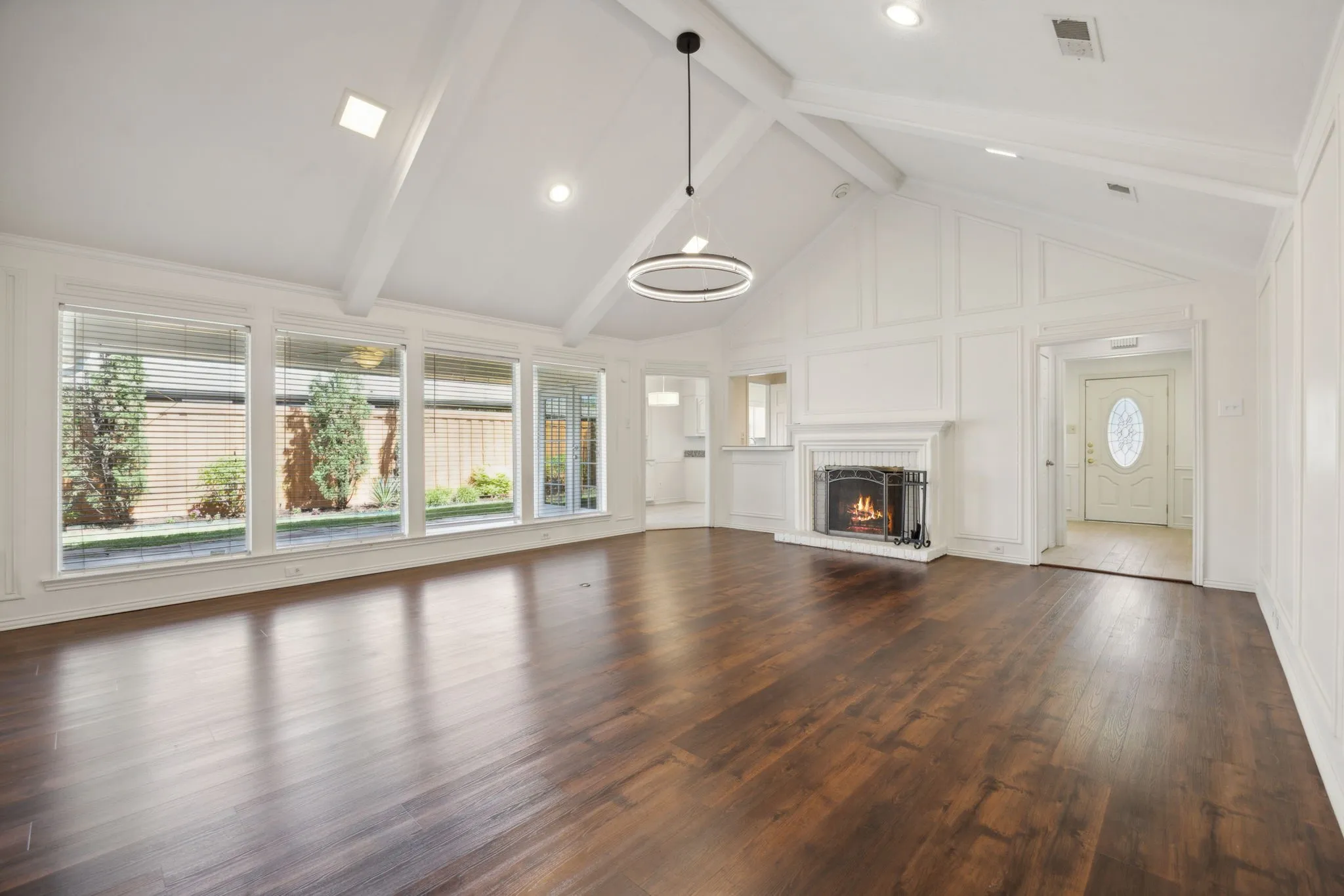 Vaulted ceiling with exposed beams, wood-finish flooring, white paneled walls, and a fireplace with a traditional mantel
