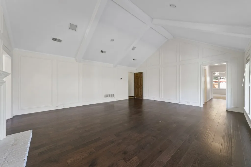 Vaulted ceiling with exposed beams, recessed lighting, dark wood-finish flooring, white paneled accent walls, and a white brick fireplace surround