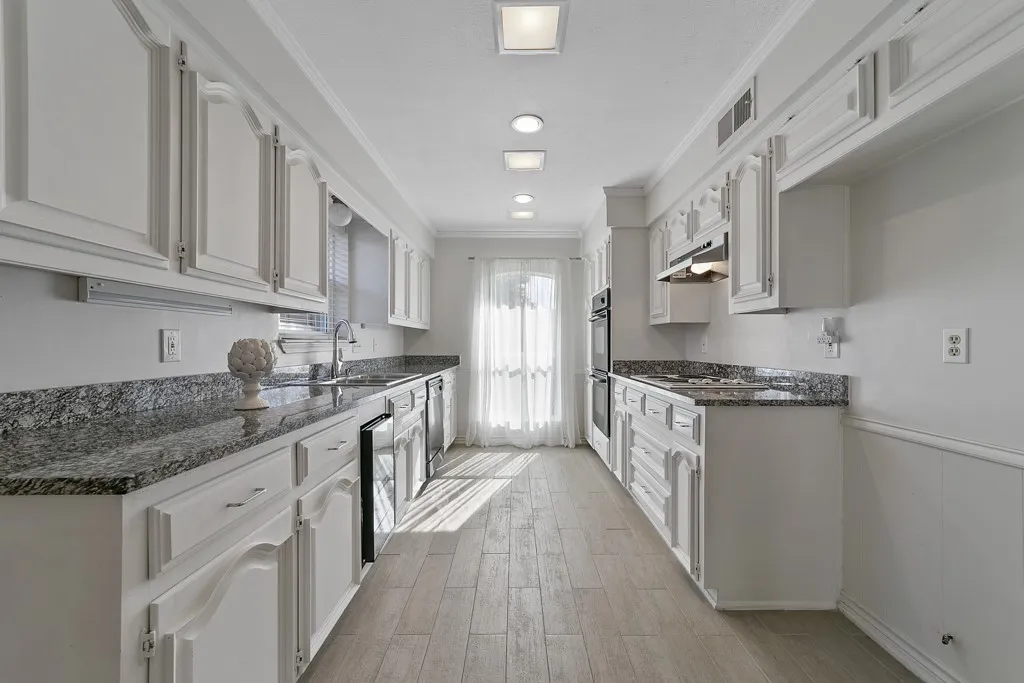 White cabinetry with decorative trim, granite countertops, tile flooring, recessed ceiling lighting, and a built-in double oven