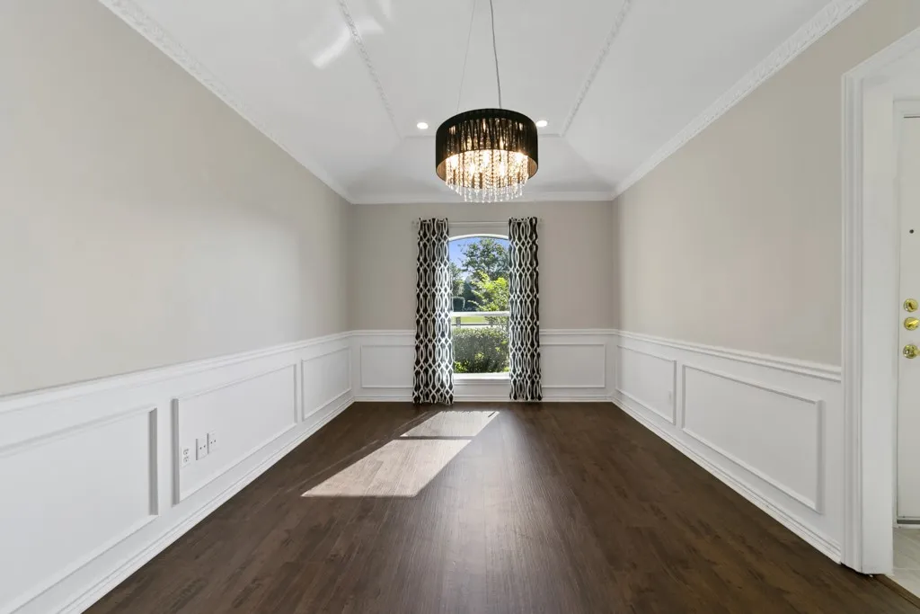 Wood-finish flooring with wainscoting, a crystal chandelier, crown molding, and a vaulted ceiling