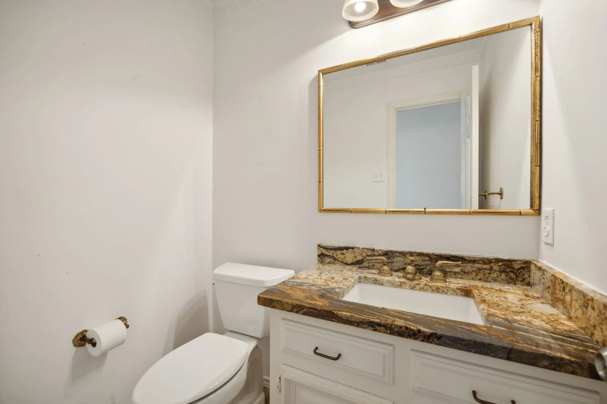White vanity with under-mount sink, detailed countertop, and gold-framed mirror