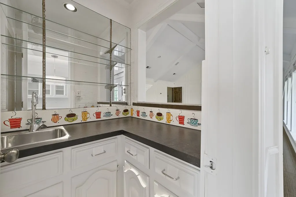 Built-in wet bar with a stainless steel sink, glass shelving, and white cabinetry