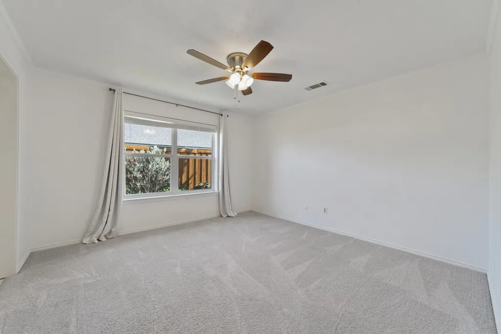 Spacious room featuring neutral carpeting, a multi-pane window, and a ceiling fan with integrated lighting