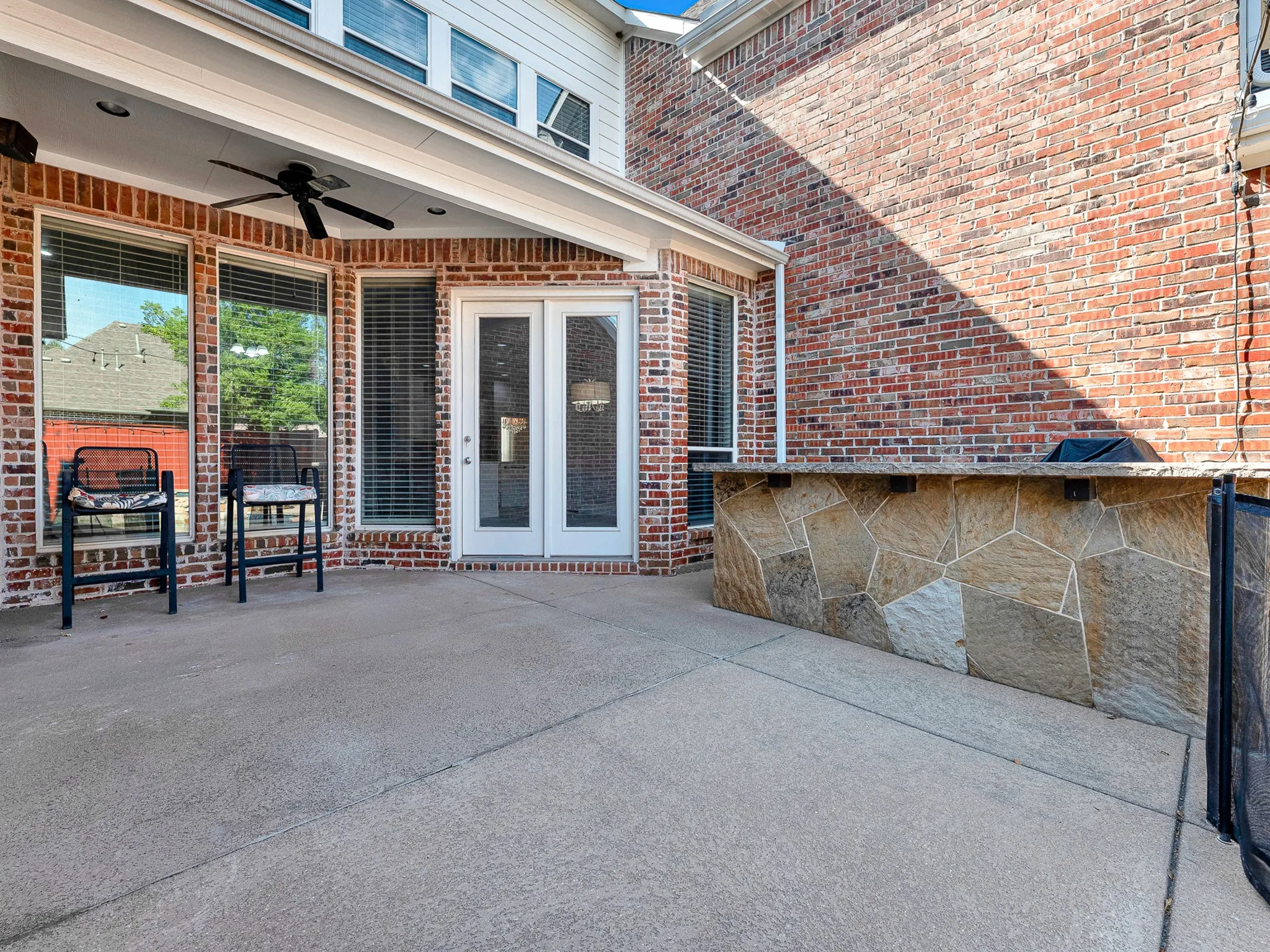 Covered patio with a ceiling fan, concrete flooring, and a built-in stone-clad outdoor kitchen