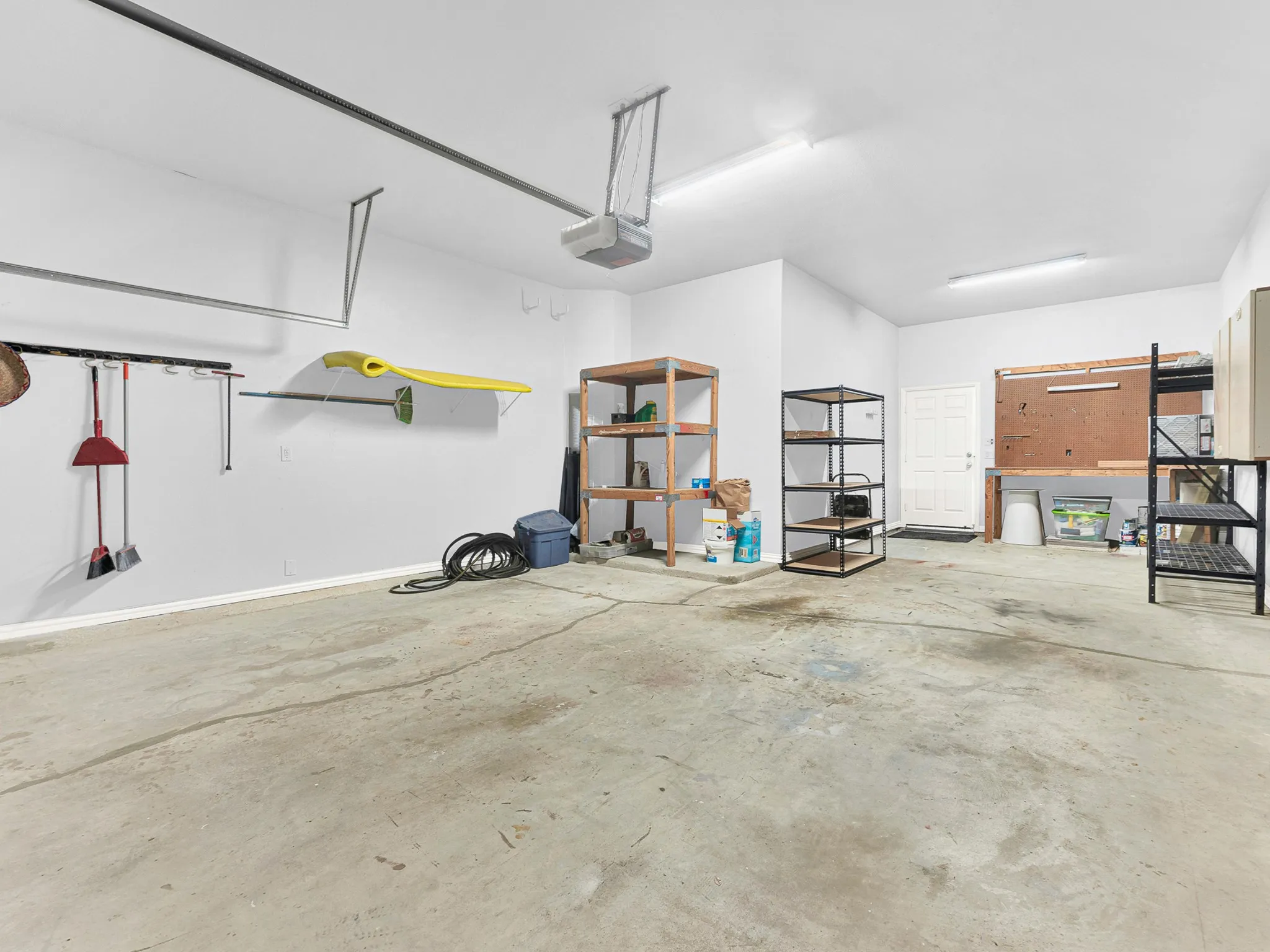 Spacious garage with exposed concrete flooring, white walls, and overhead fluorescent lighting