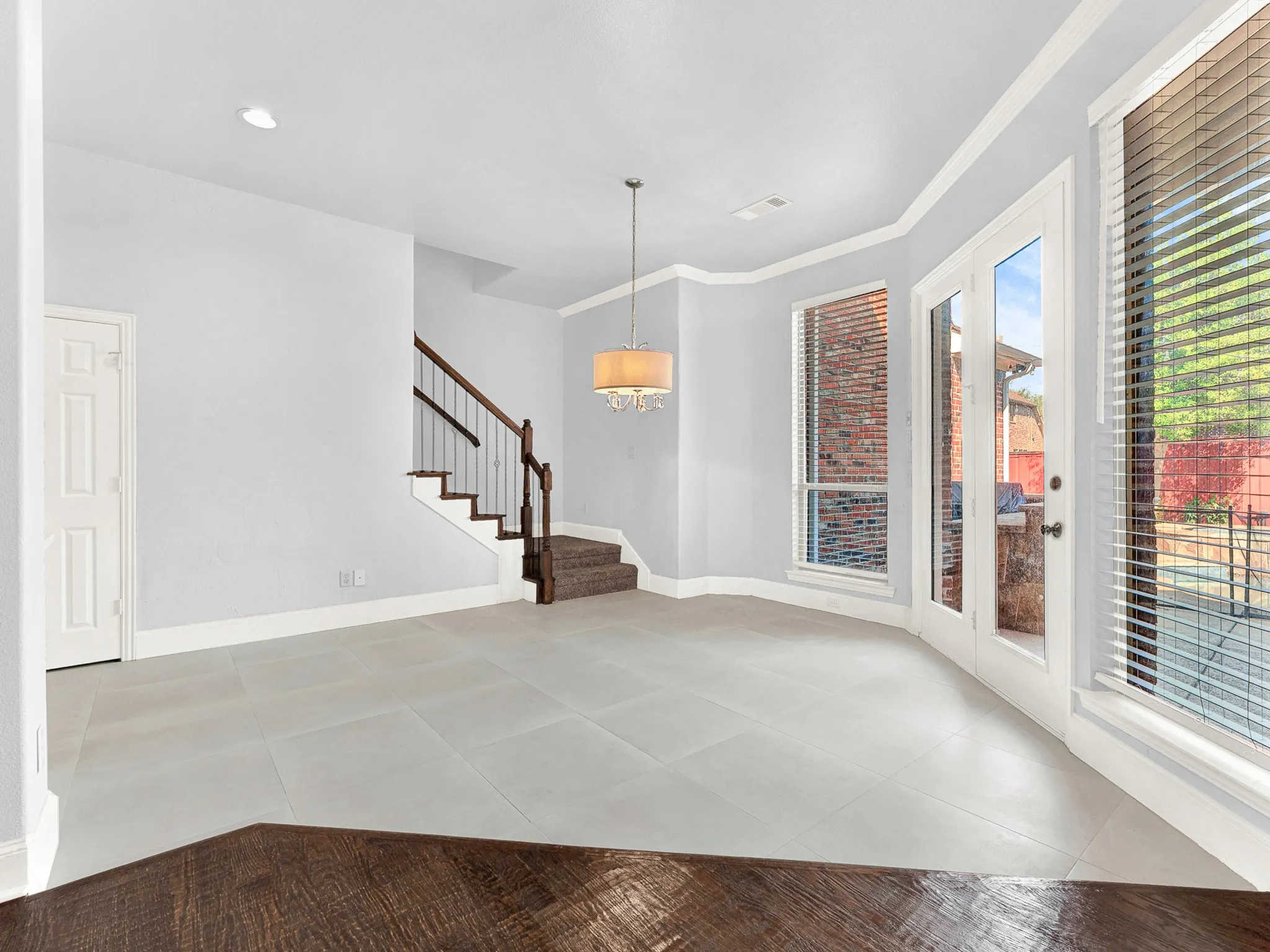 Light gray tiled flooring, built-in staircase with wood railing, double French doors, large windows, and a chandelier lighting fixture