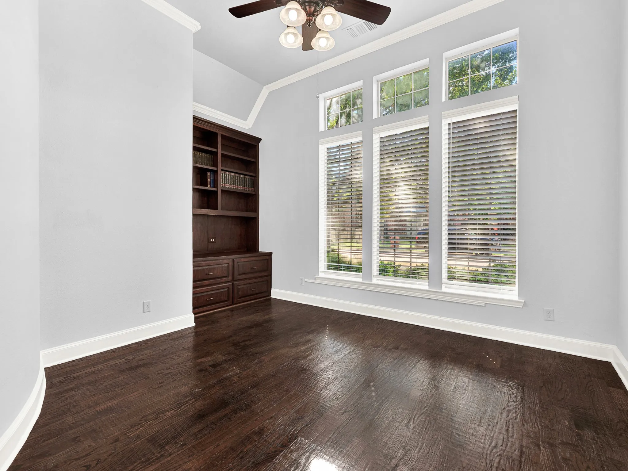 Built-in dark wood cabinetry with shelving, dark wood-finish flooring, and multiple tall windows with blinds