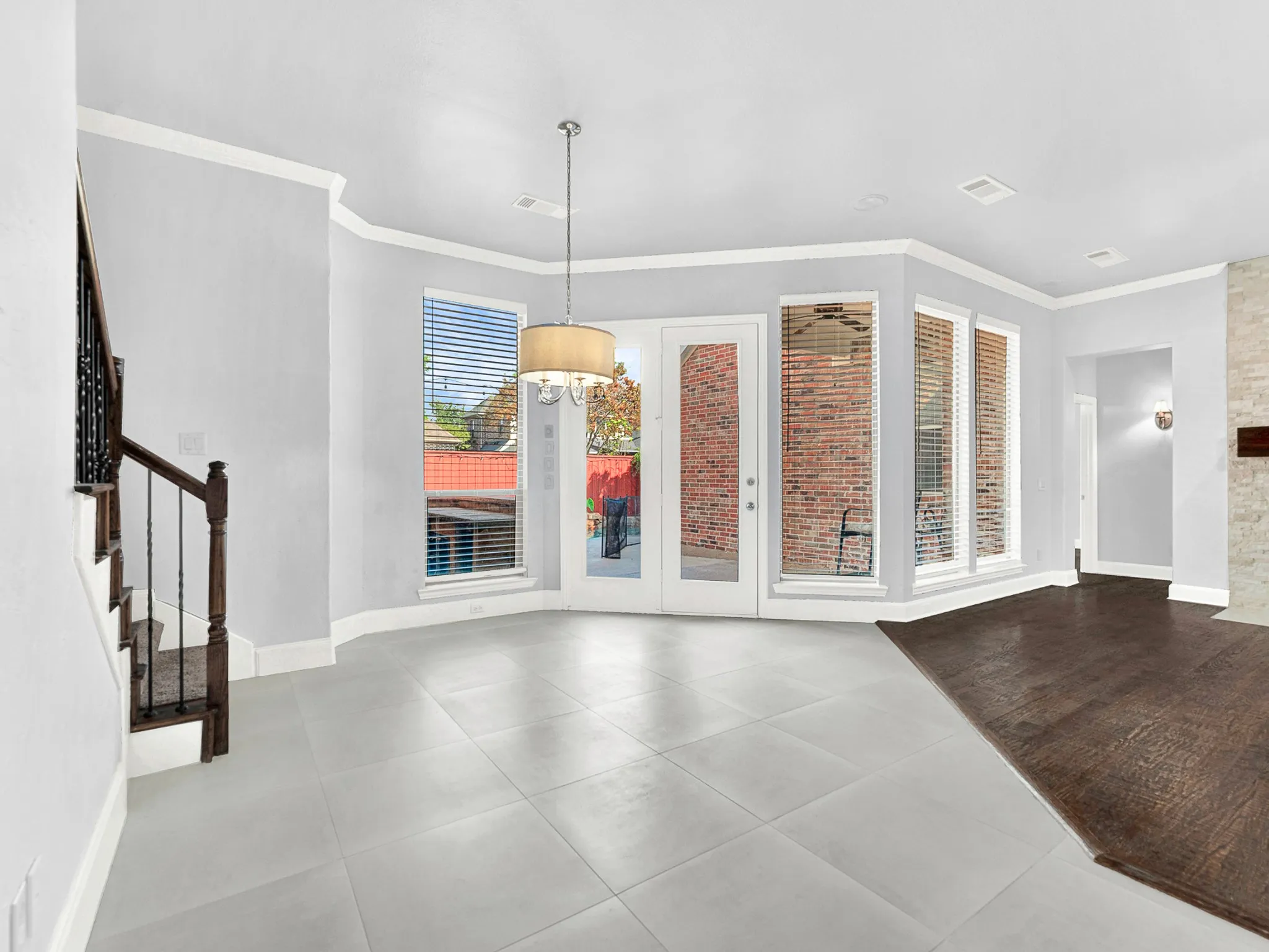 Bay window feature with multiple panes, light gray tile flooring, French doors, wood-finish flooring, and a built-in staircase with dark wood and wrought iron balusters