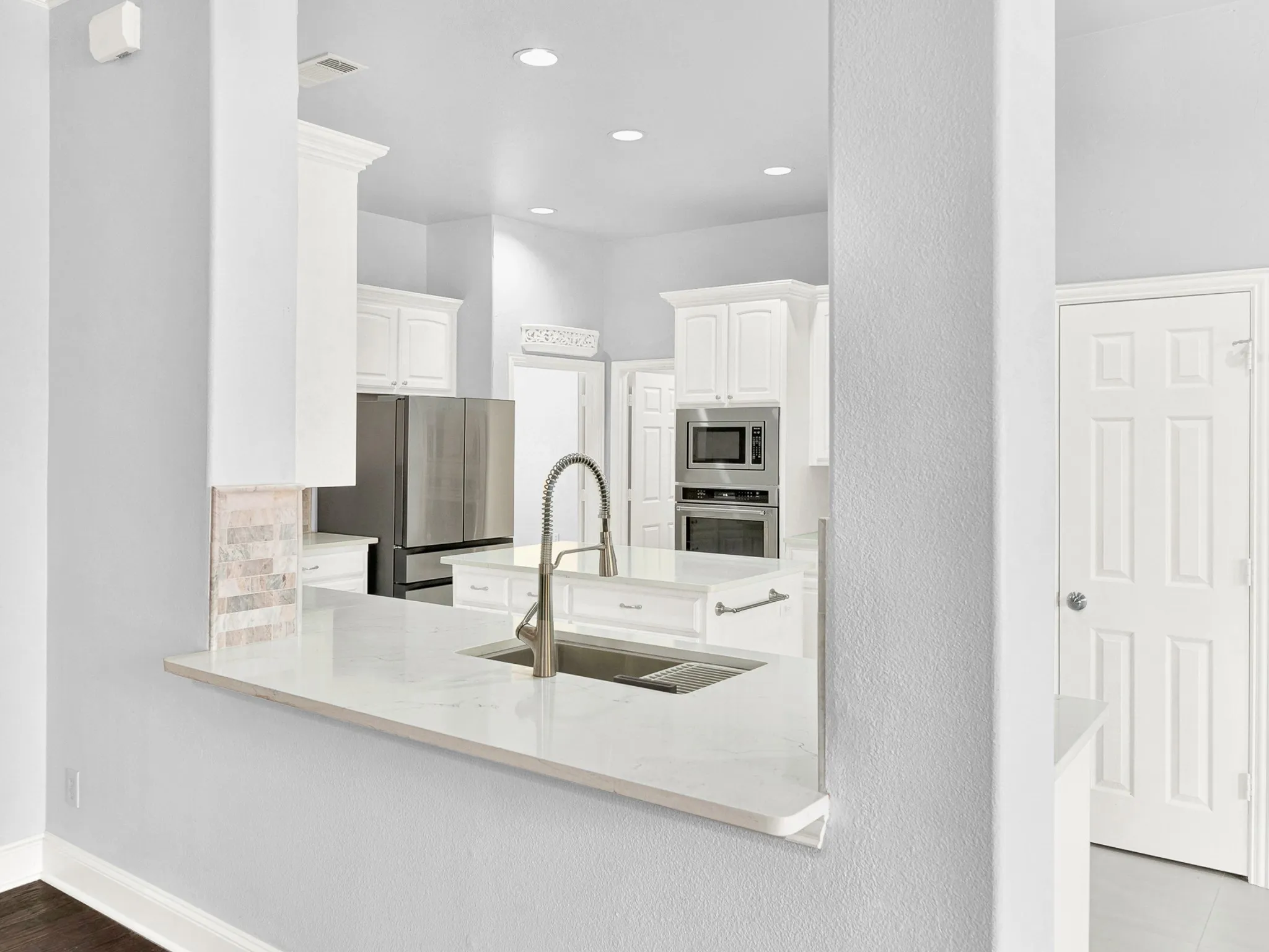 Kitchen pass-through featuring a white countertop with an undermount sink and a gooseneck faucet