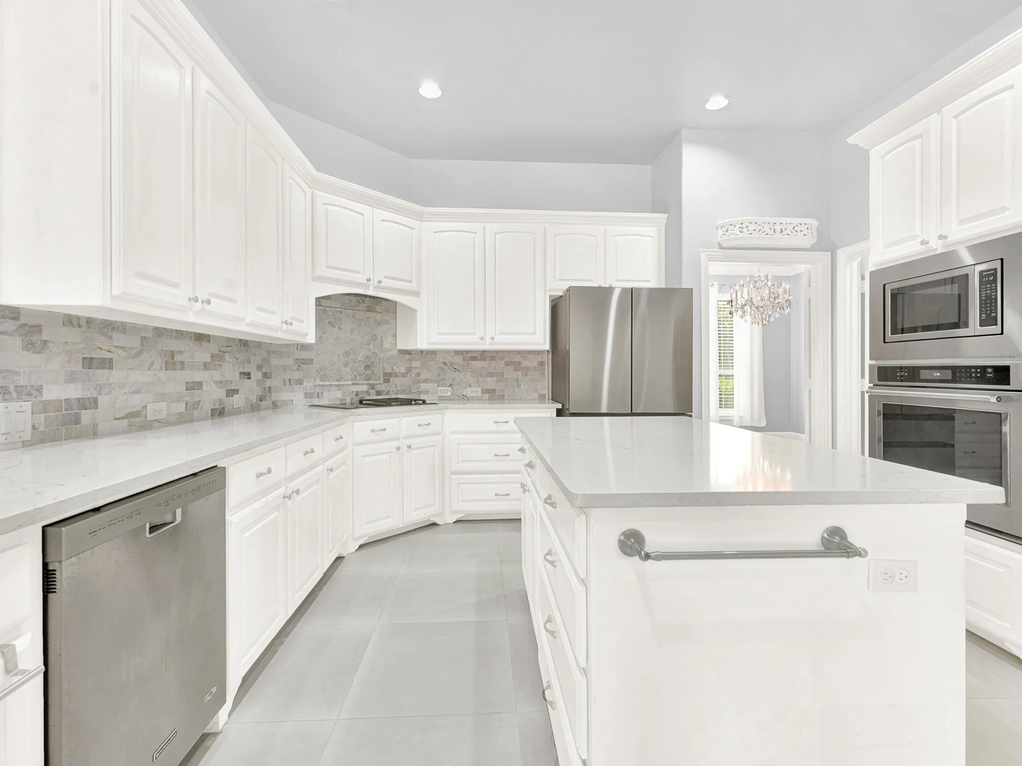 White cabinetry with hardware, light-toned countertops, a tile backsplash, stainless steel appliances, and a central island