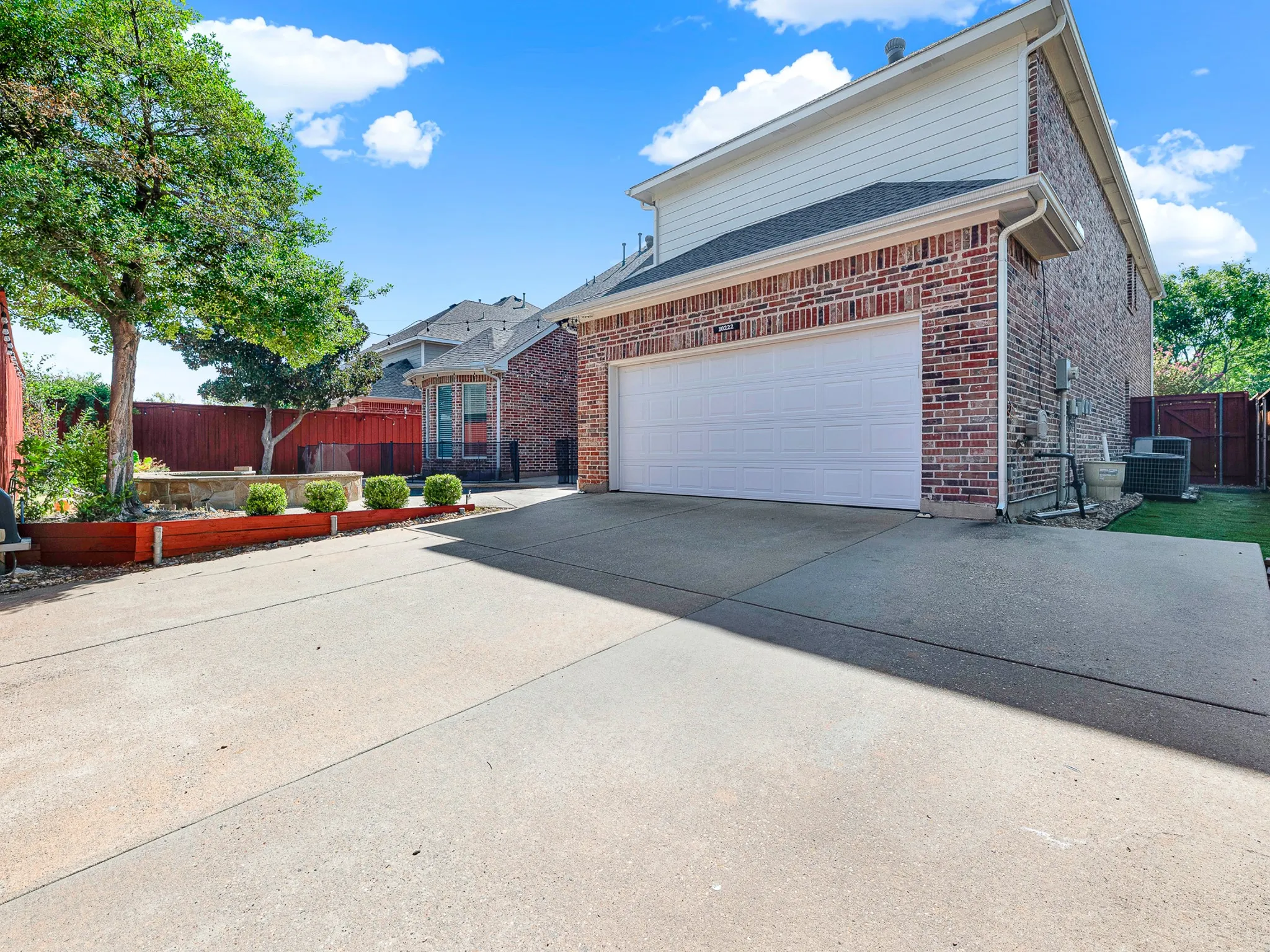 Brick facade with white siding, attached garage, concrete driveway, and a fenced yard
