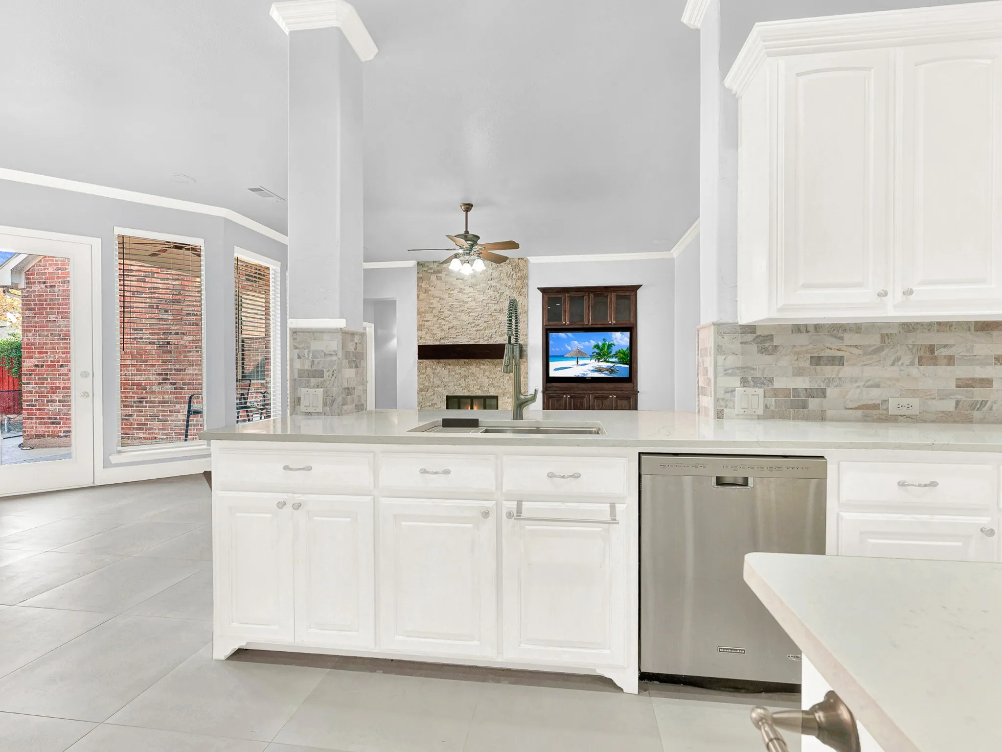 White cabinetry, light countertops, subway tile backsplash, stainless steel dishwasher, and a centered island sink with a gooseneck faucet