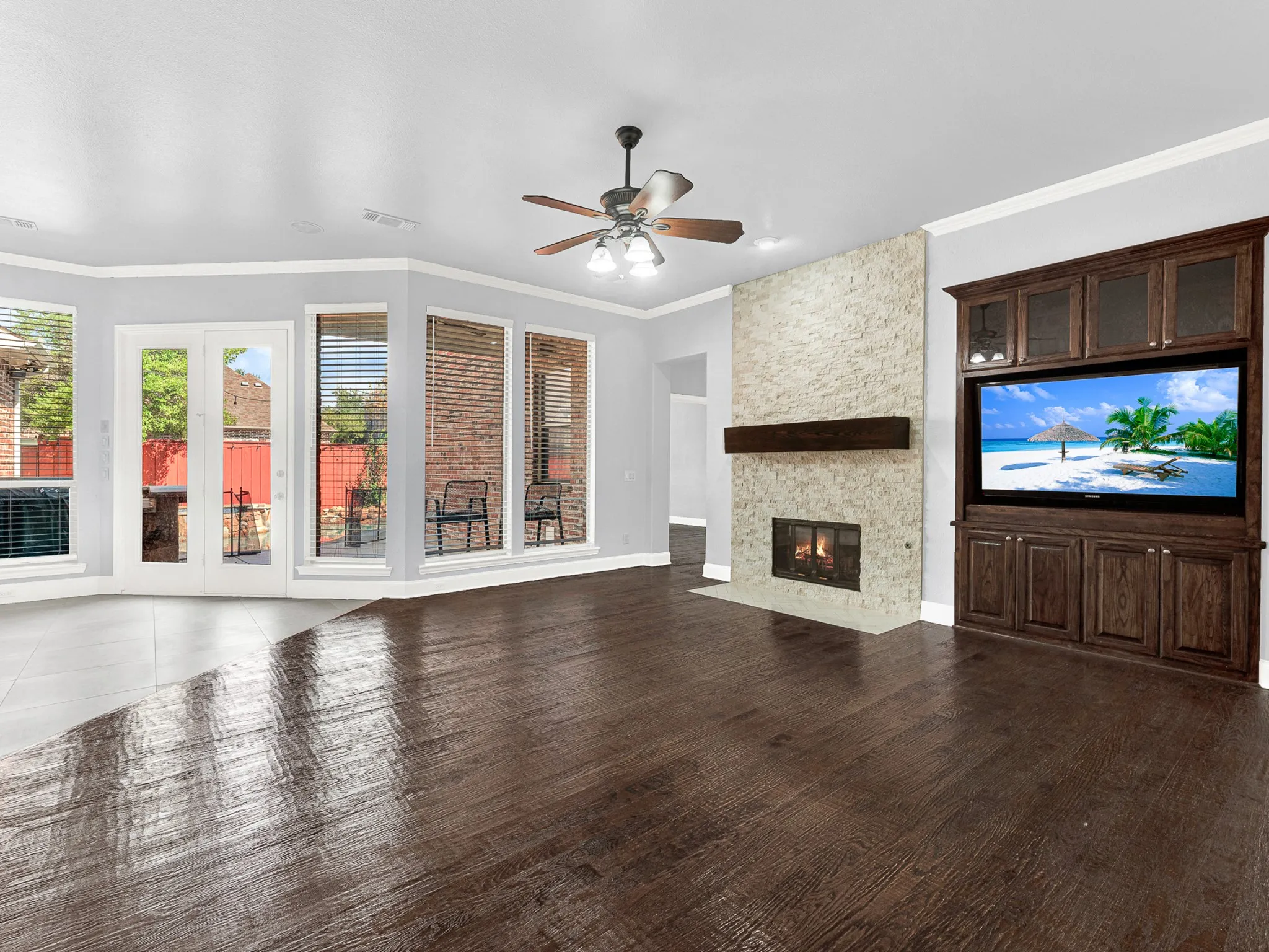 Expansive living area with wood-finish flooring, a stone-clad fireplace, and a built-in entertainment center