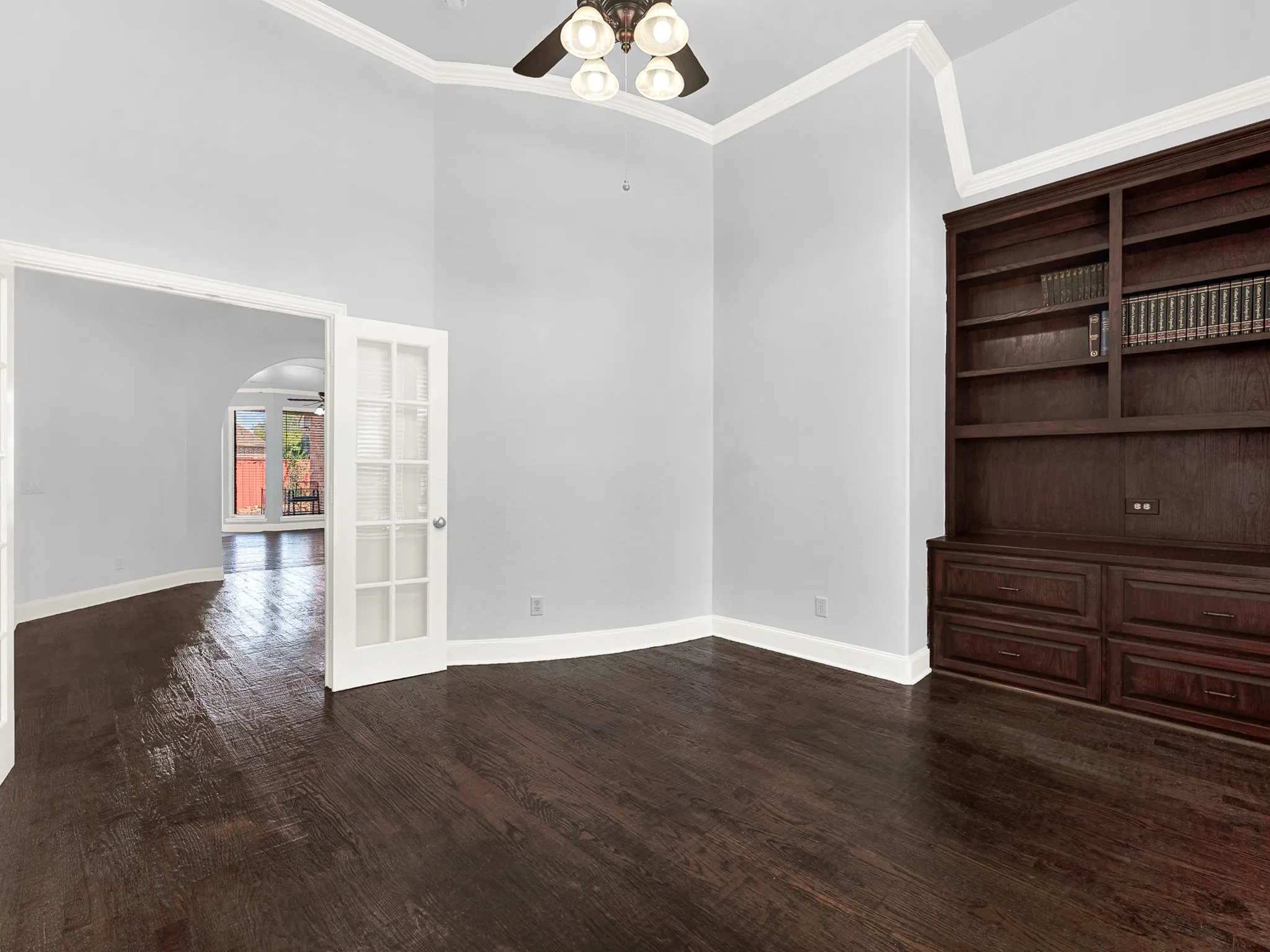 Dark wood-finish flooring, built-in shelving with lower cabinetry, and crown molding