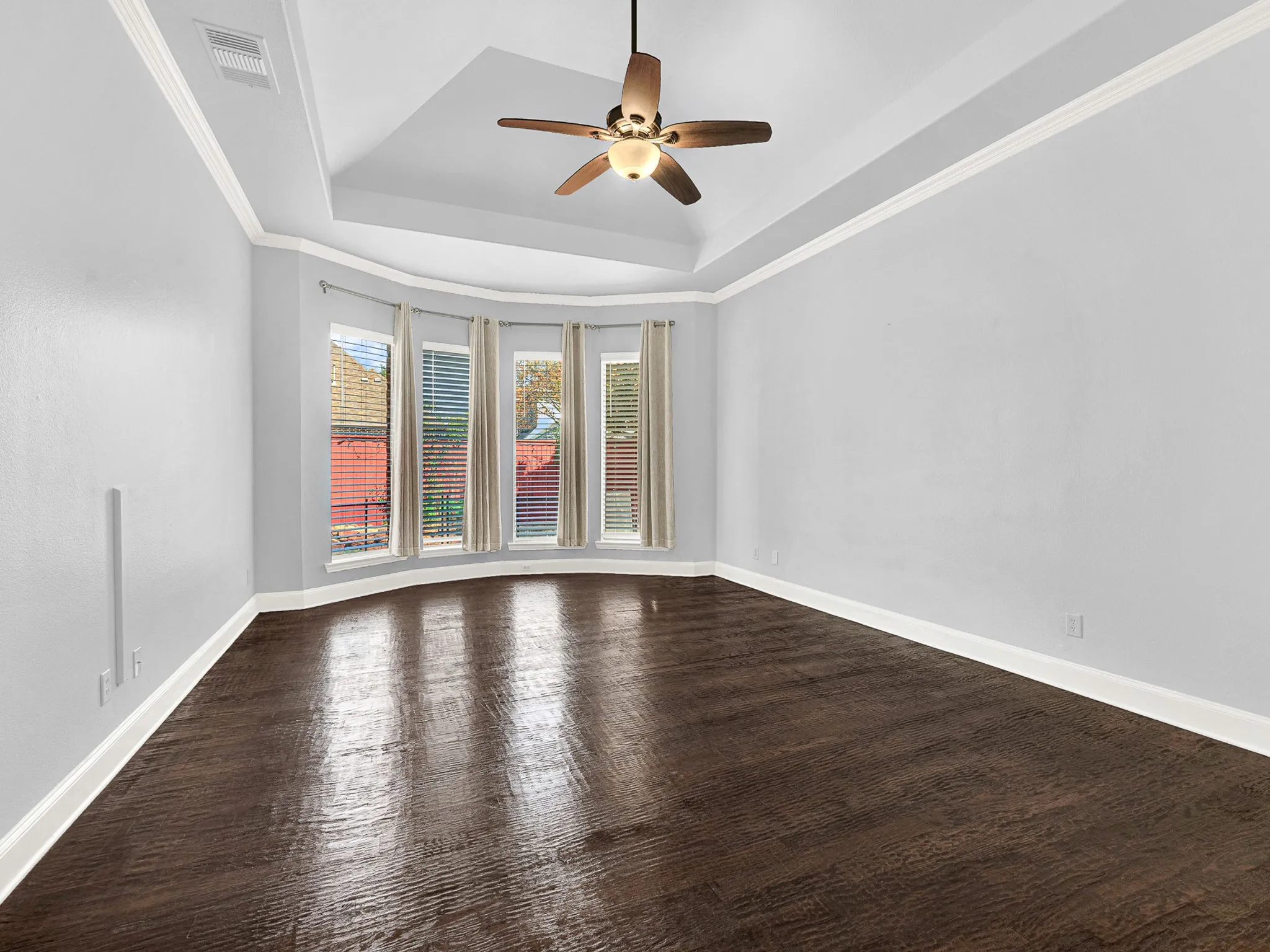 Tray ceiling with crown molding, wood-finish flooring, ceiling fan, and bay windows