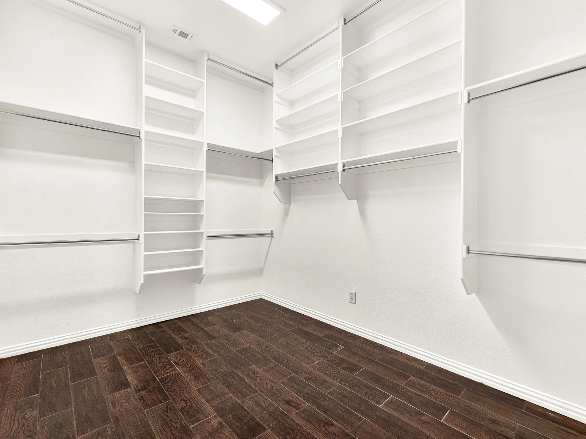 Custom closet system with built-in shelving, multiple hanging rods, and dark wood-finish flooring