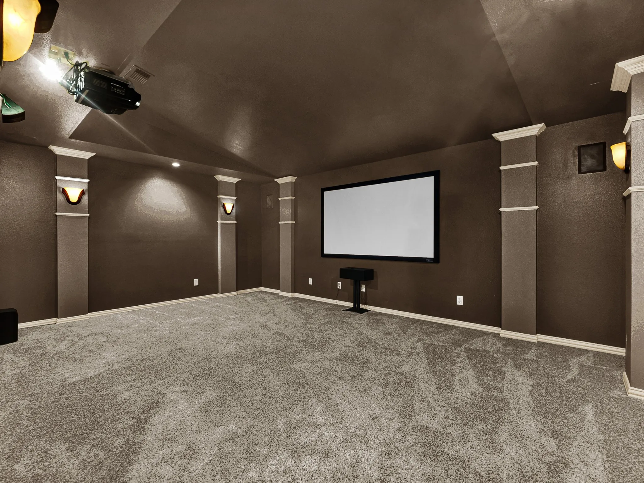 Dedicated media room featuring a large projection screen, wall-mounted projector, recessed lighting, and wall sconces