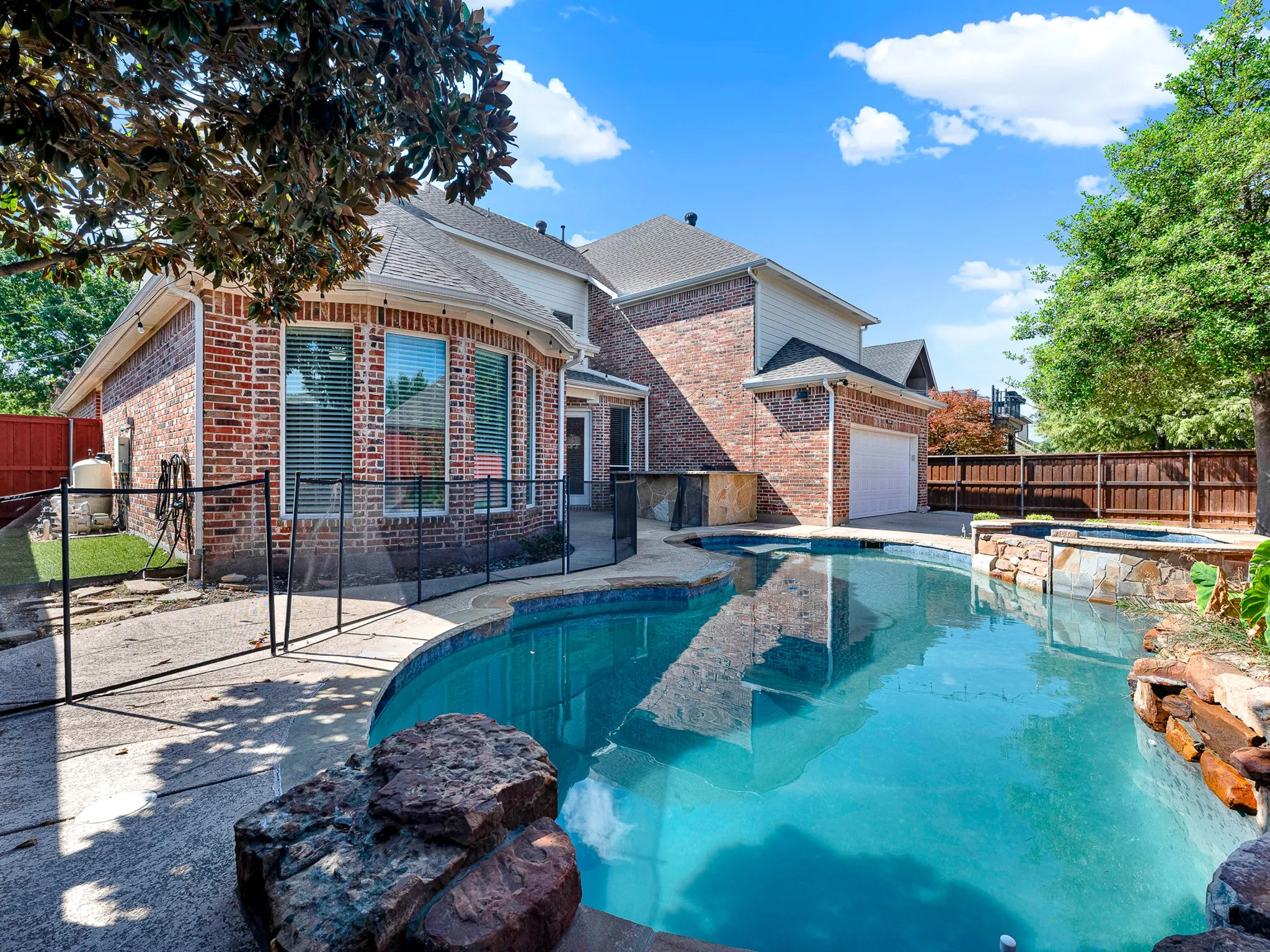Brick exterior with a multi-level roofline, featuring a built-in swimming pool, integrated spa, and an outdoor kitchen area