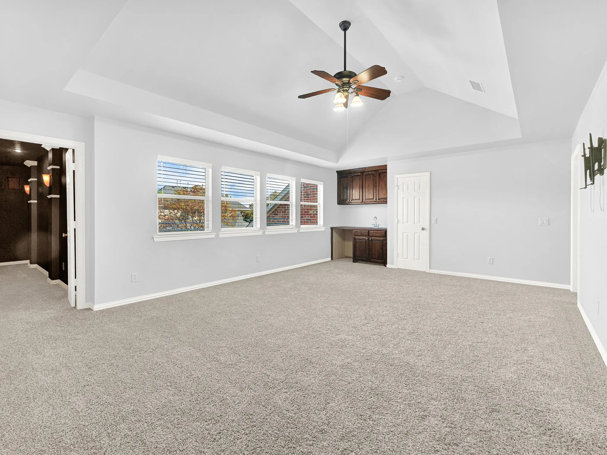 Tray ceiling with ceiling fan, built-in cabinetry with a sink, light gray walls, and carpet flooring