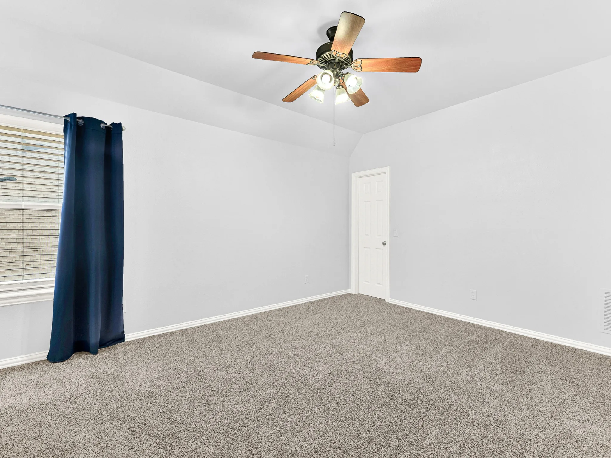 Vaulted ceiling with a ceiling fan light fixture, light gray walls, gray carpet flooring, and a white window with blinds