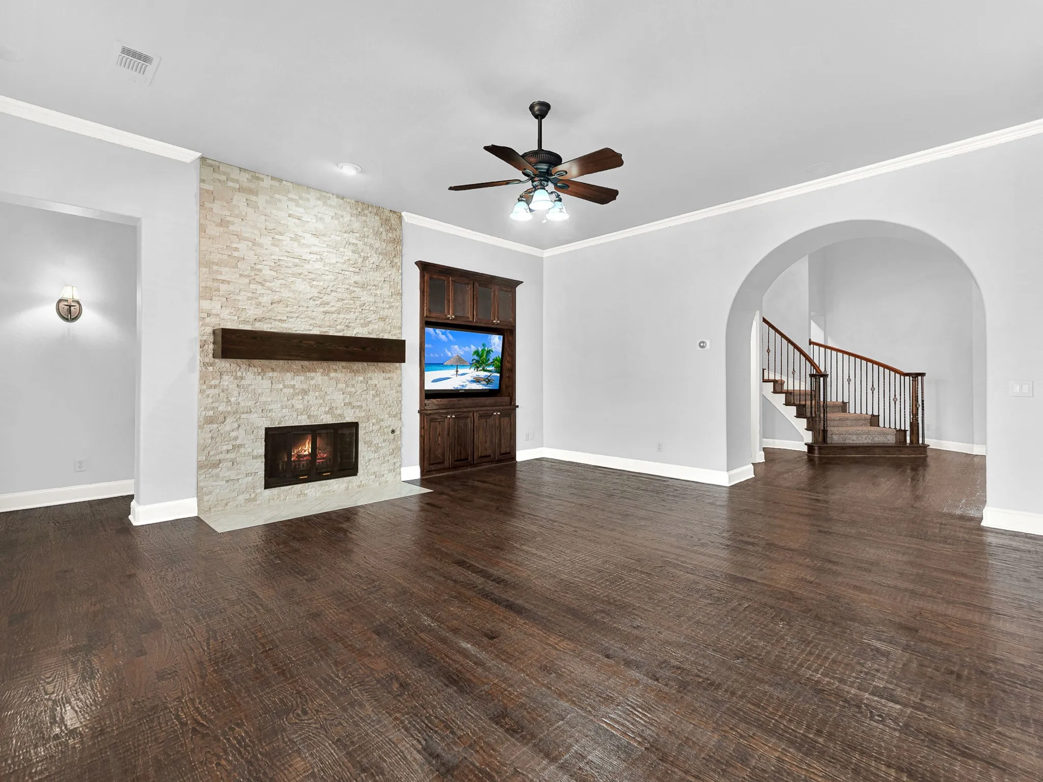 Stacked stone fireplace with a wood-beam mantel, built-in media cabinetry, wood-finish flooring, and an arched entryway