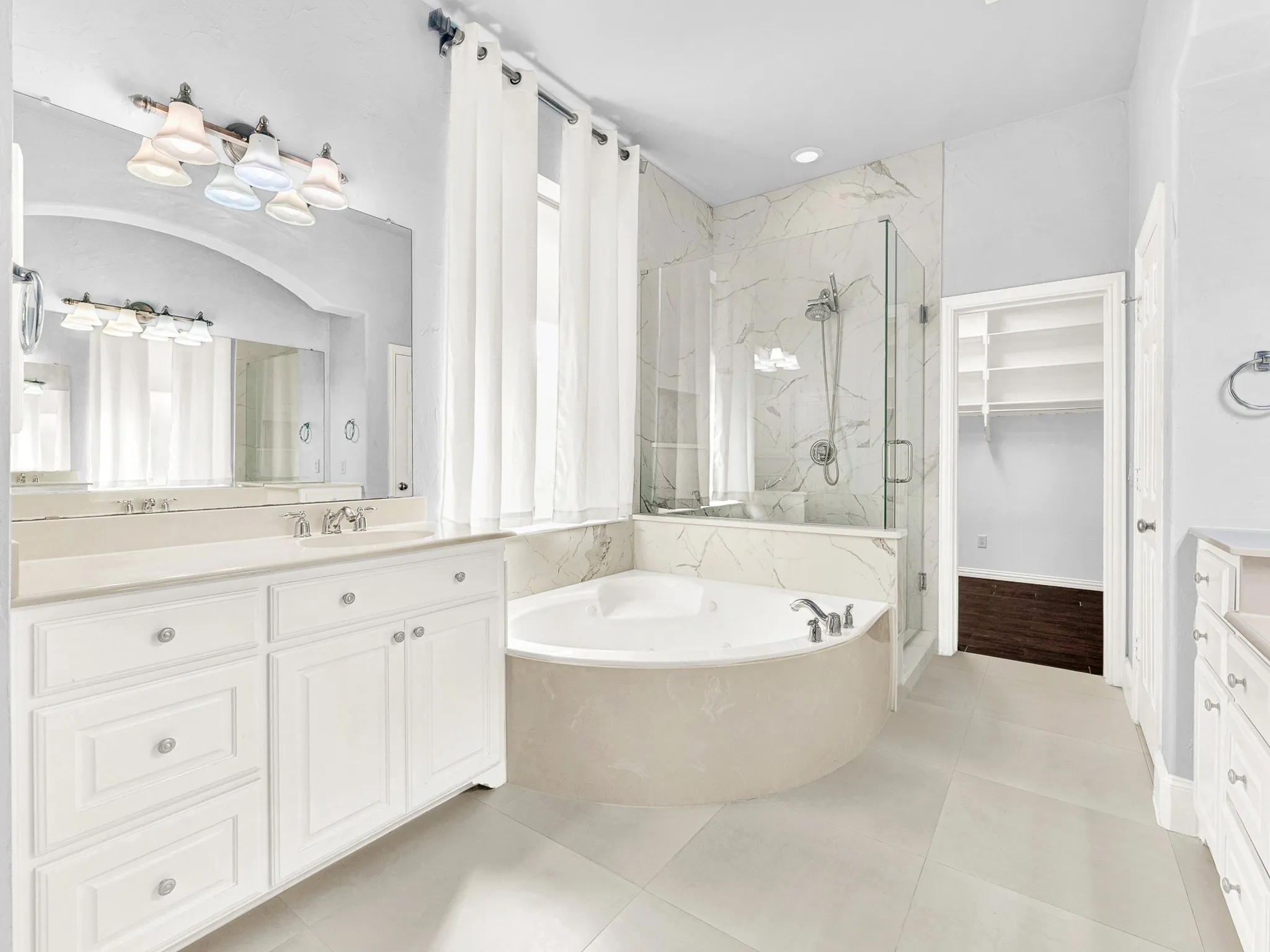 Spacious bathroom featuring a built-in jetted tub, glass-enclosed shower, dual vanities with integrated sinks, and neutral tile flooring